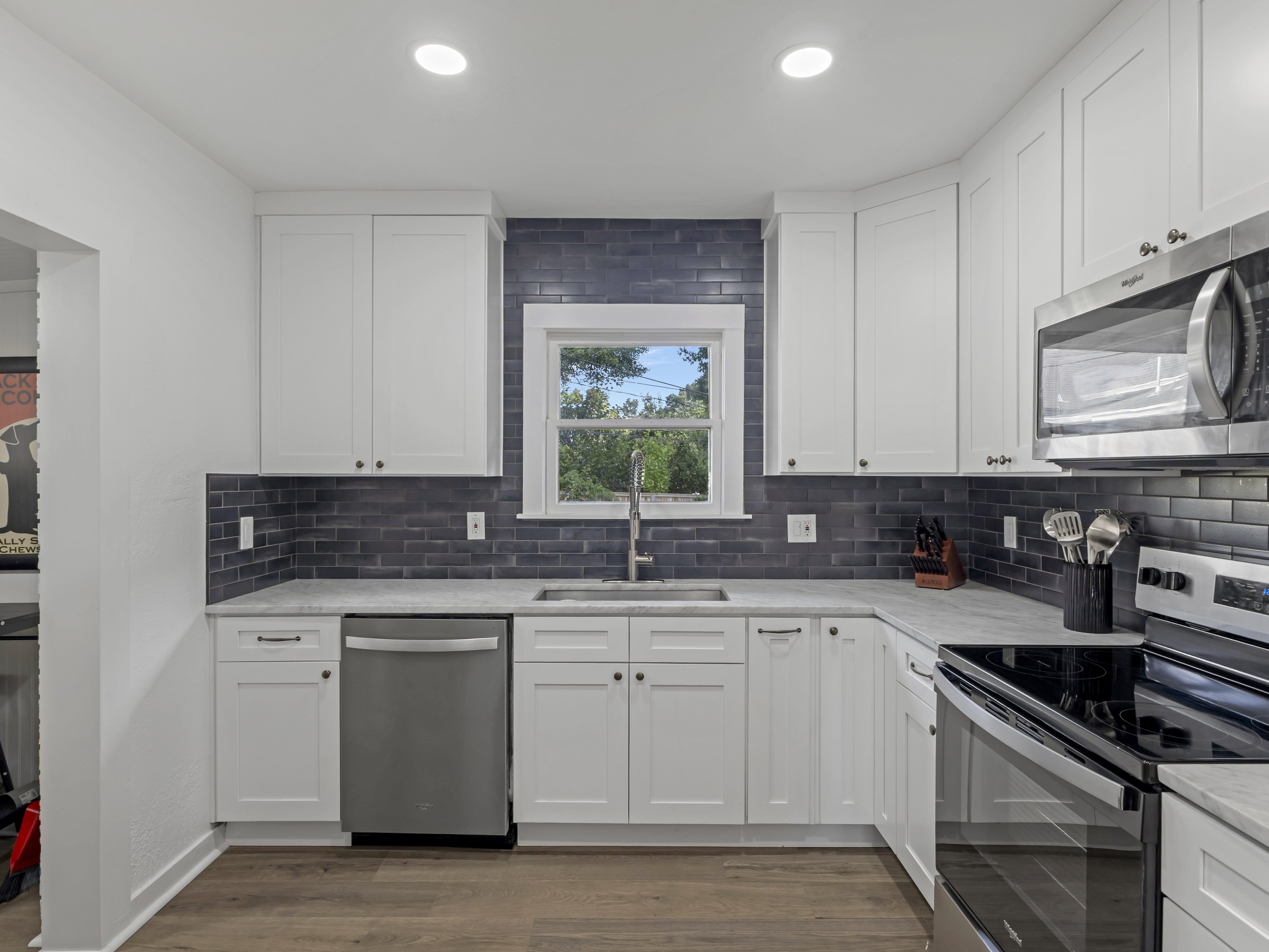 Modern kitchen featuring white shaker-style cabinetry, a dark subway tile backsplash, light-toned countertops, stainless steel appliances, and recessed lighting