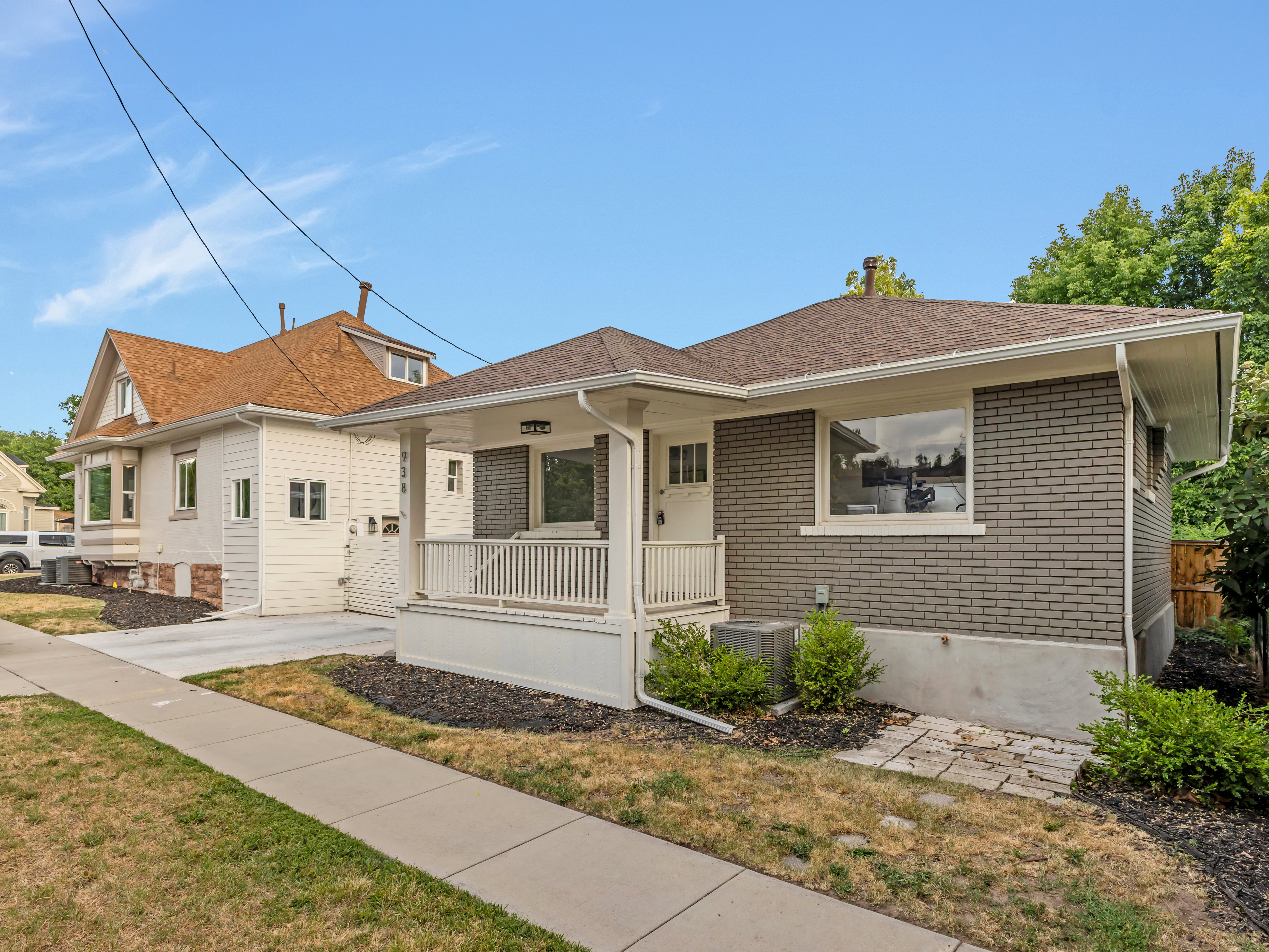Contemporary home featuring a gray brick facade, white trim, and a covered front porch with white railings