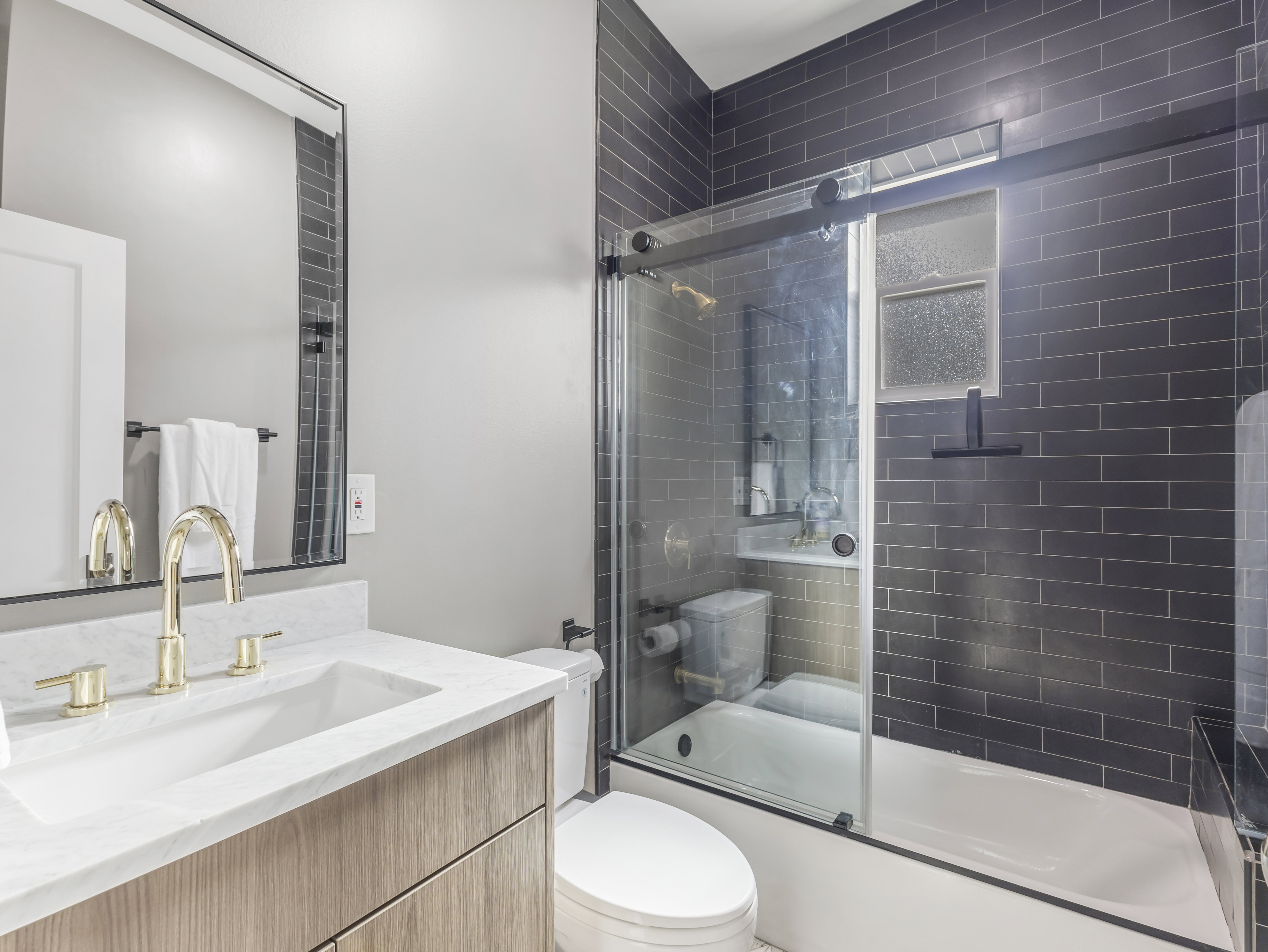 Contemporary bathroom featuring a wood-finish vanity with a white countertop and brass-finish fixtures