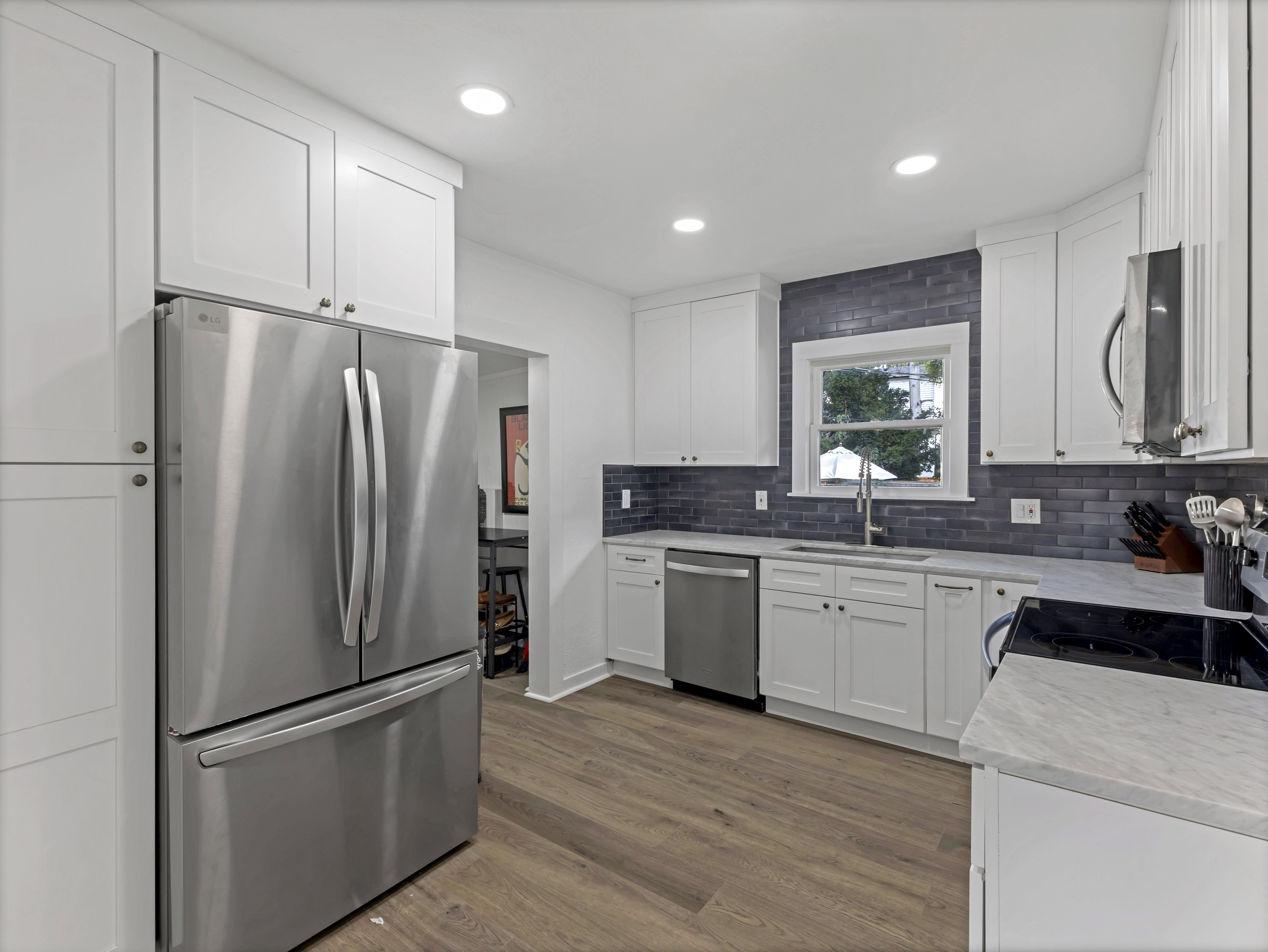 Kitchen featuring white shaker-style cabinetry, stainless steel appliances, a dark subway tile backsplash, light-toned countertops, and wood-finish flooring