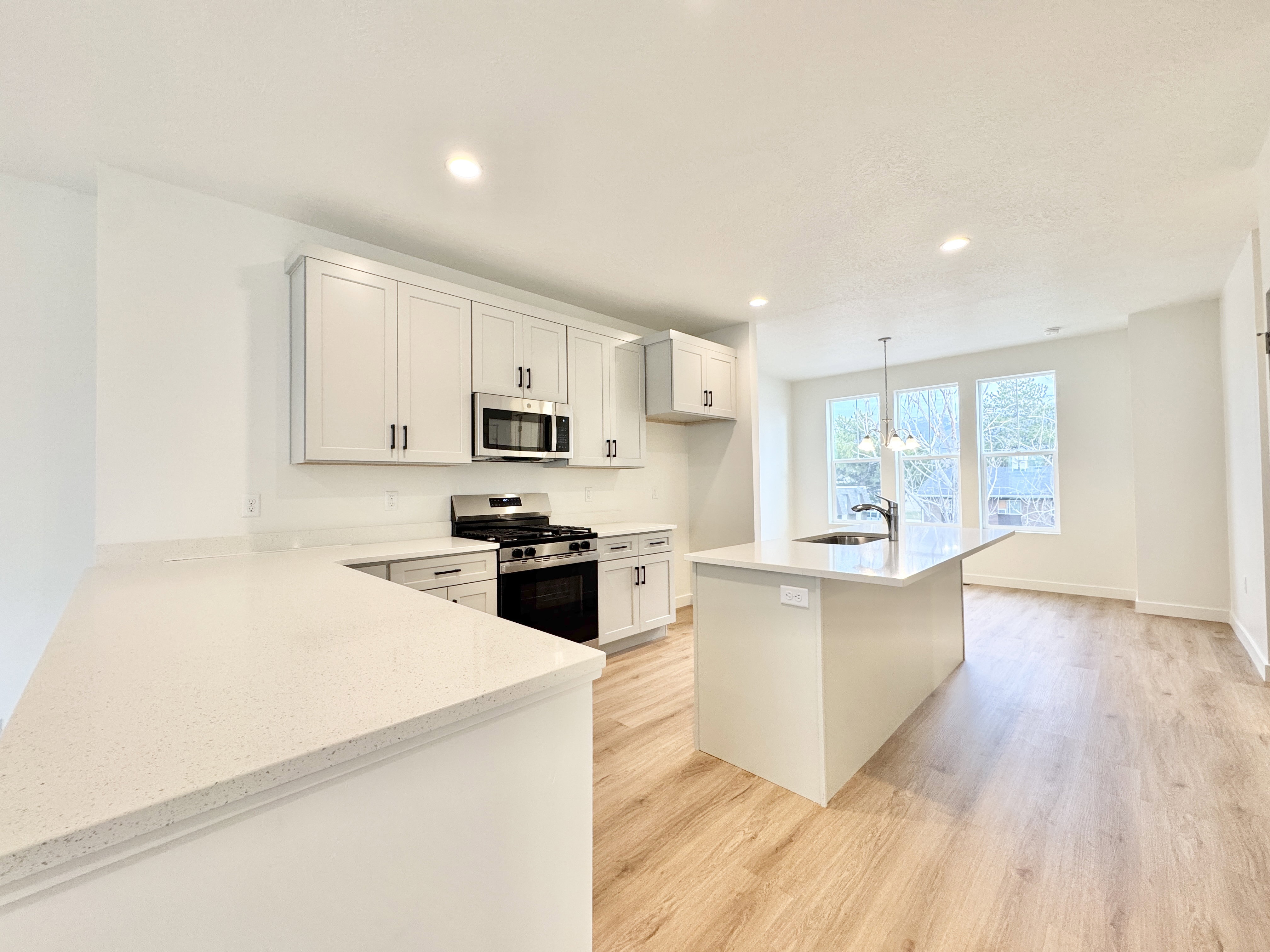 Open-concept kitchen featuring light wood-finish flooring, white cabinetry with dark hardware, stainless steel appliances, and white stone countertops