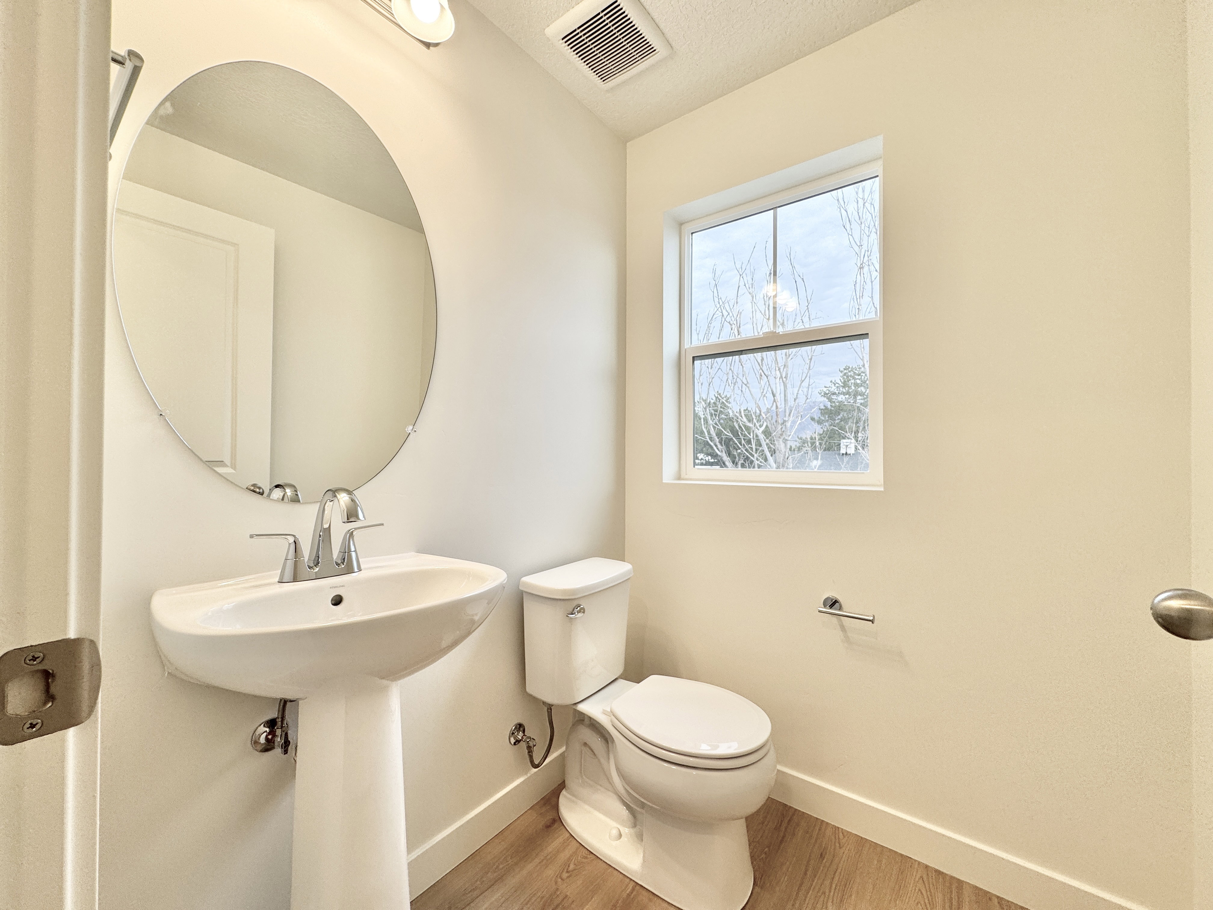 Pedestal sink with chrome faucet, oval frameless mirror, and overhead vanity lighting