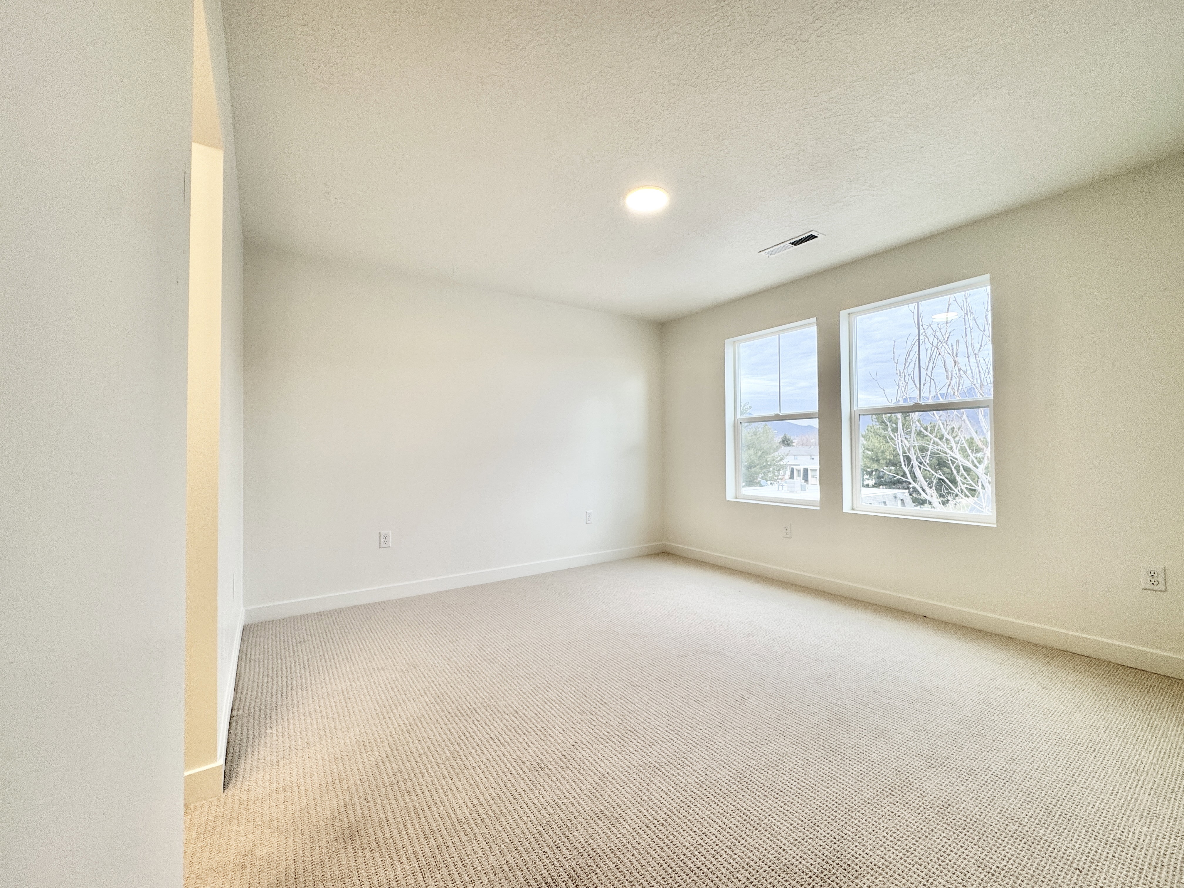 Carpeted interior space featuring two large windows providing natural light, a recessed ceiling light, and white baseboards