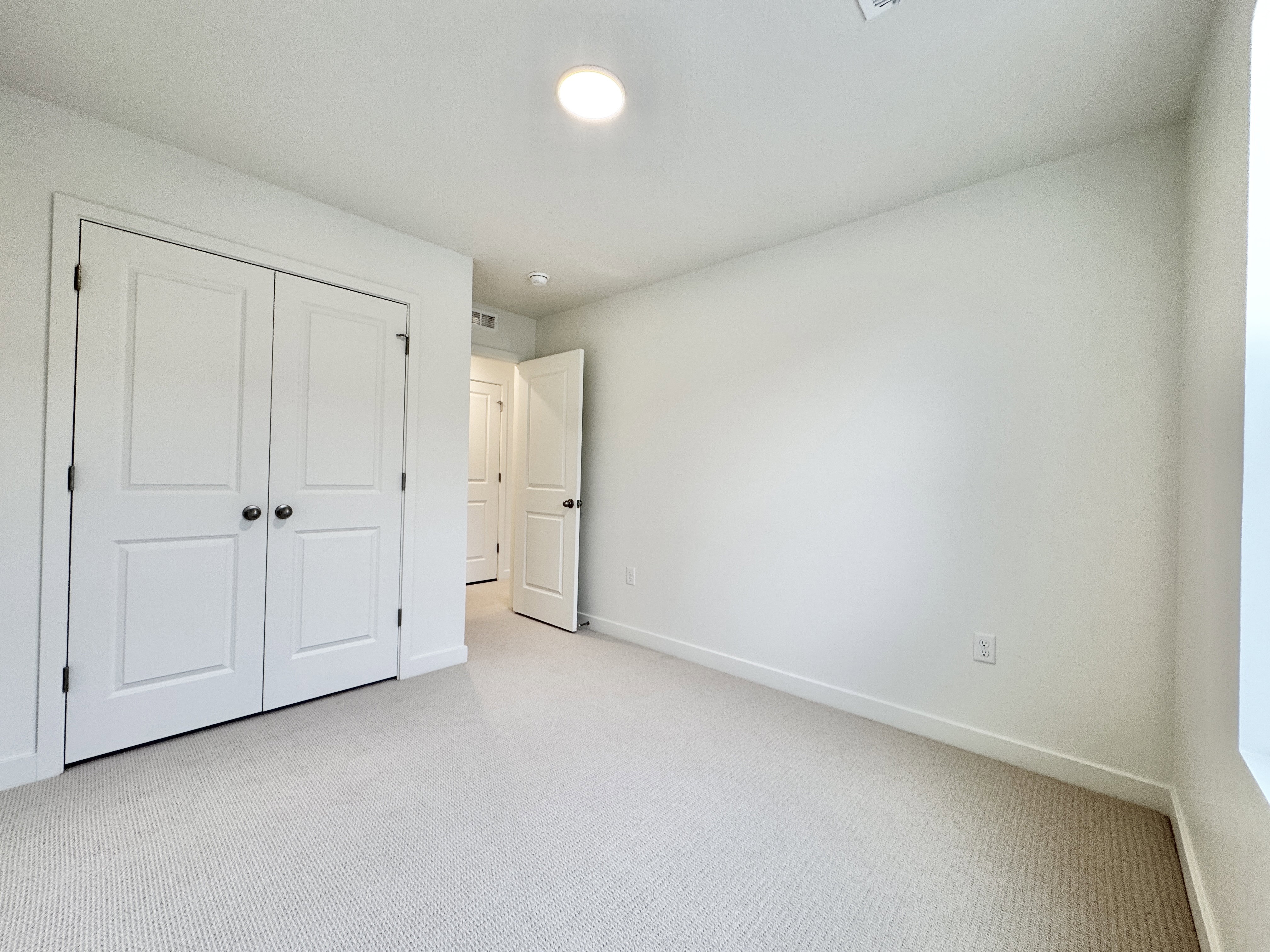 Room featuring light-colored carpet, white walls, and a pair of white bifold closet doors with dark hardware