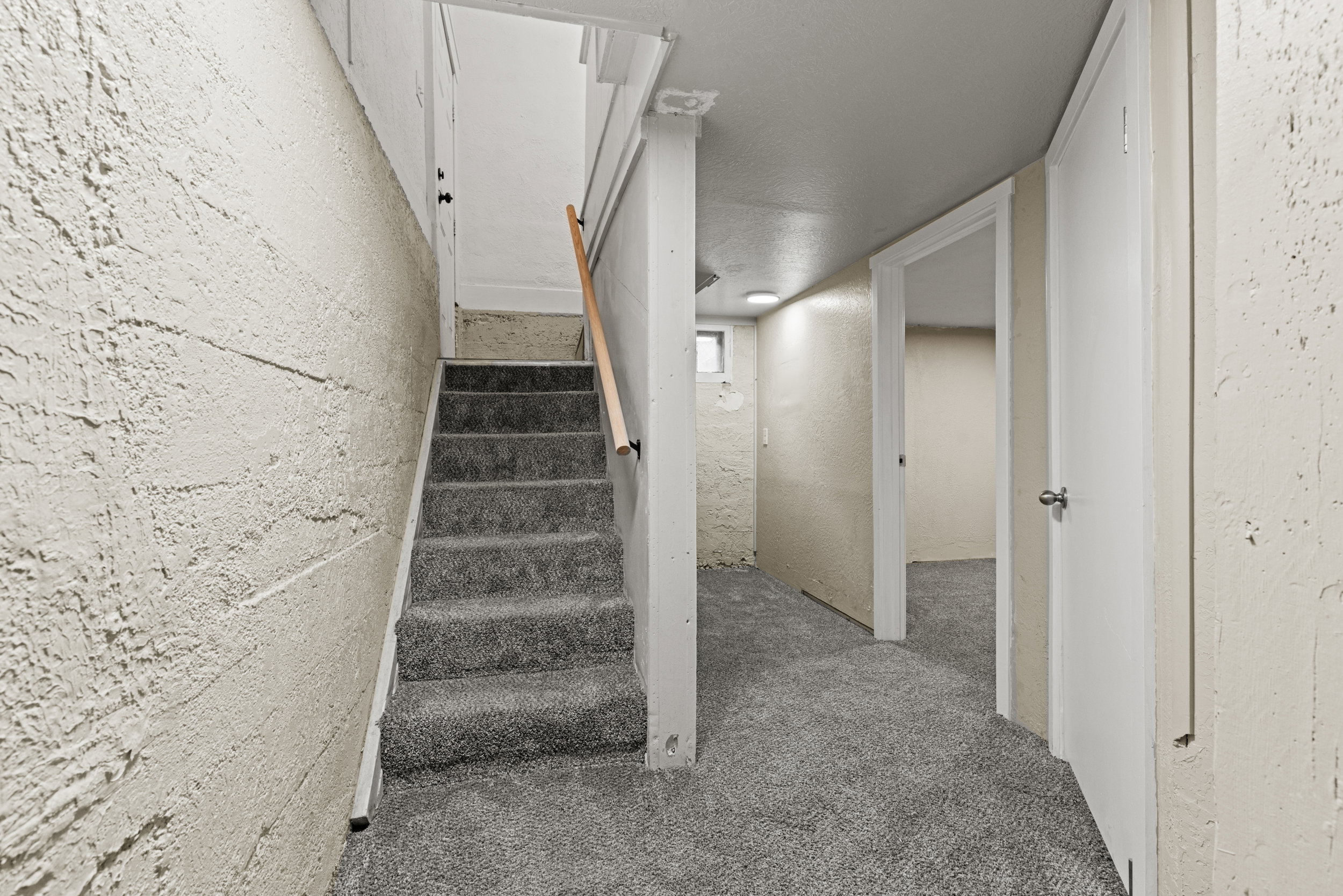 Carpeted staircase with a wood-finish handrail, leading to a textured wall