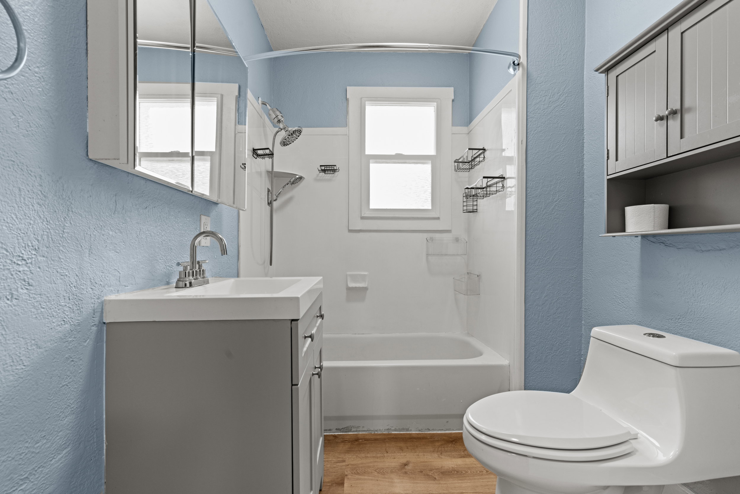 Bathroom featuring a vanity with integrated sink, chrome faucet, medicine cabinet, and wood-finish flooring