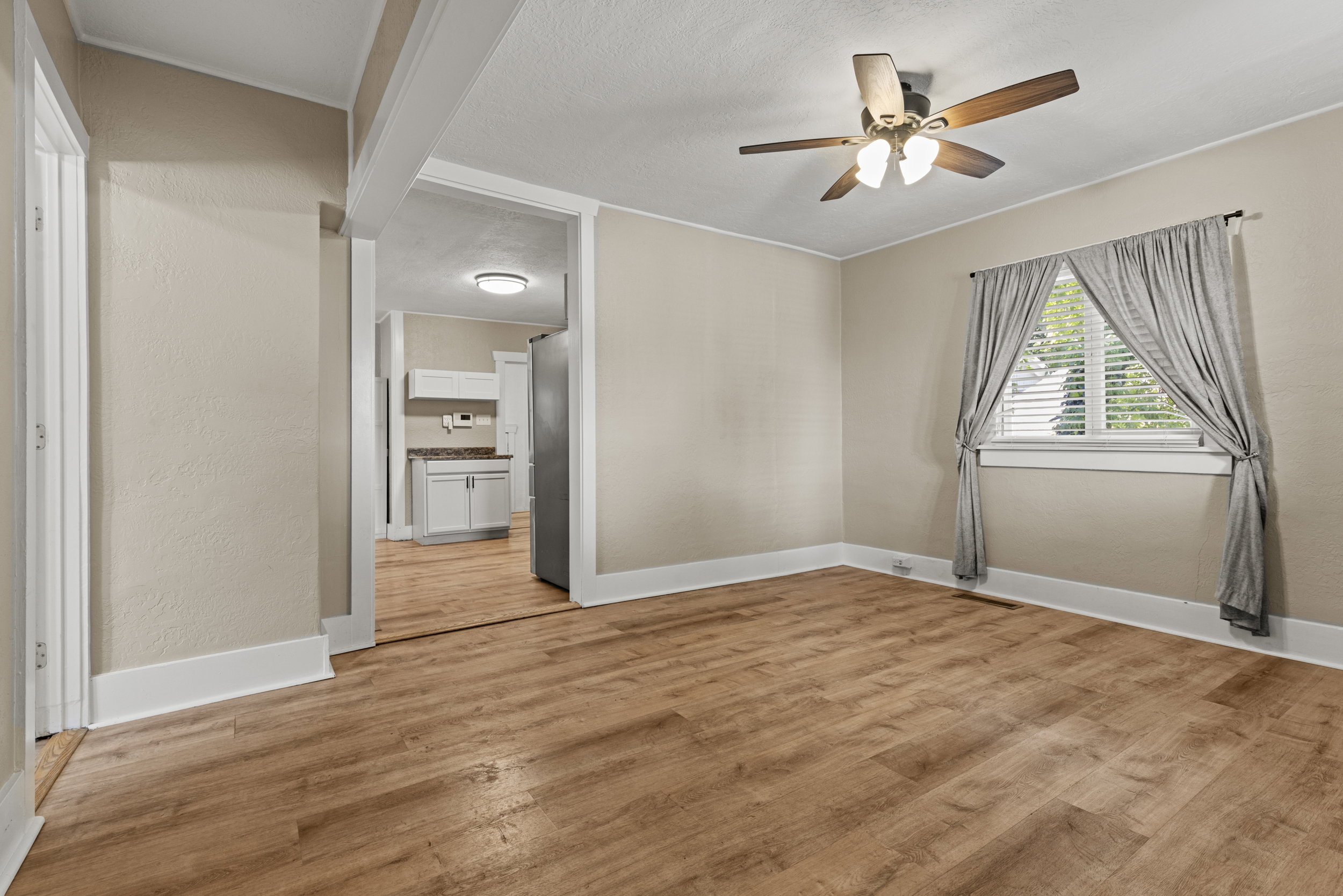 Open living area featuring wood-finish flooring, neutral paint, a ceiling fan, and a window with blinds