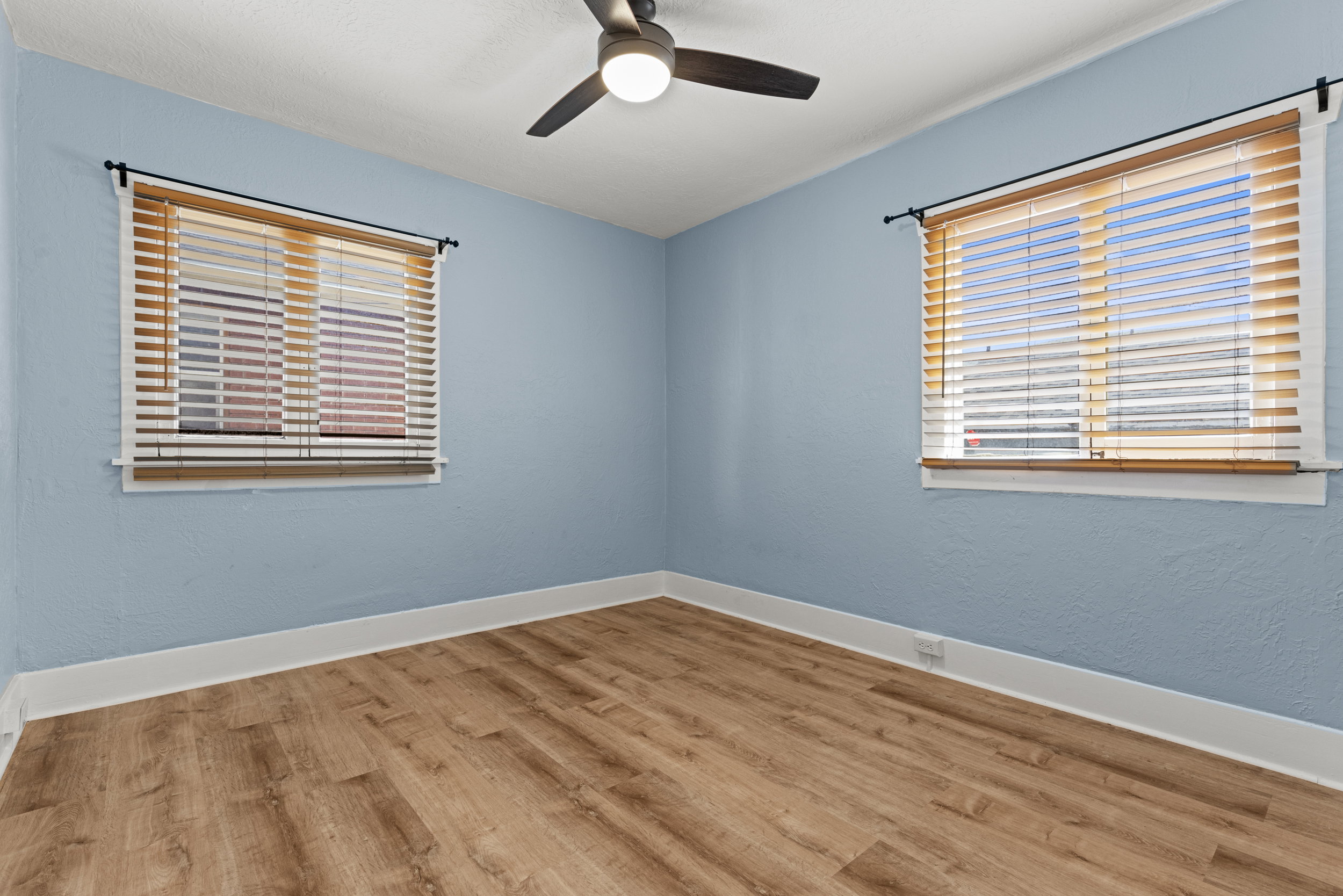 Interior room featuring wood-finish flooring, two windows with blinds, a ceiling fan with integrated lighting, and white baseboards