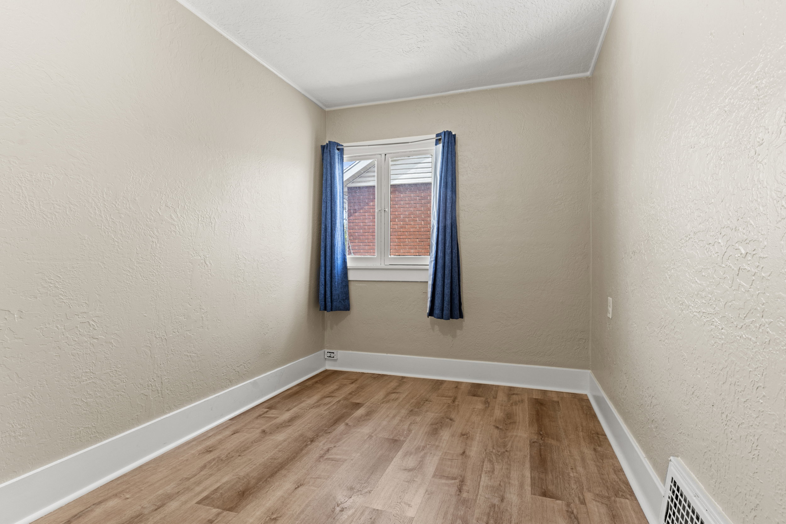 Neutral-toned room with wood-finish flooring, white baseboards, and textured walls
