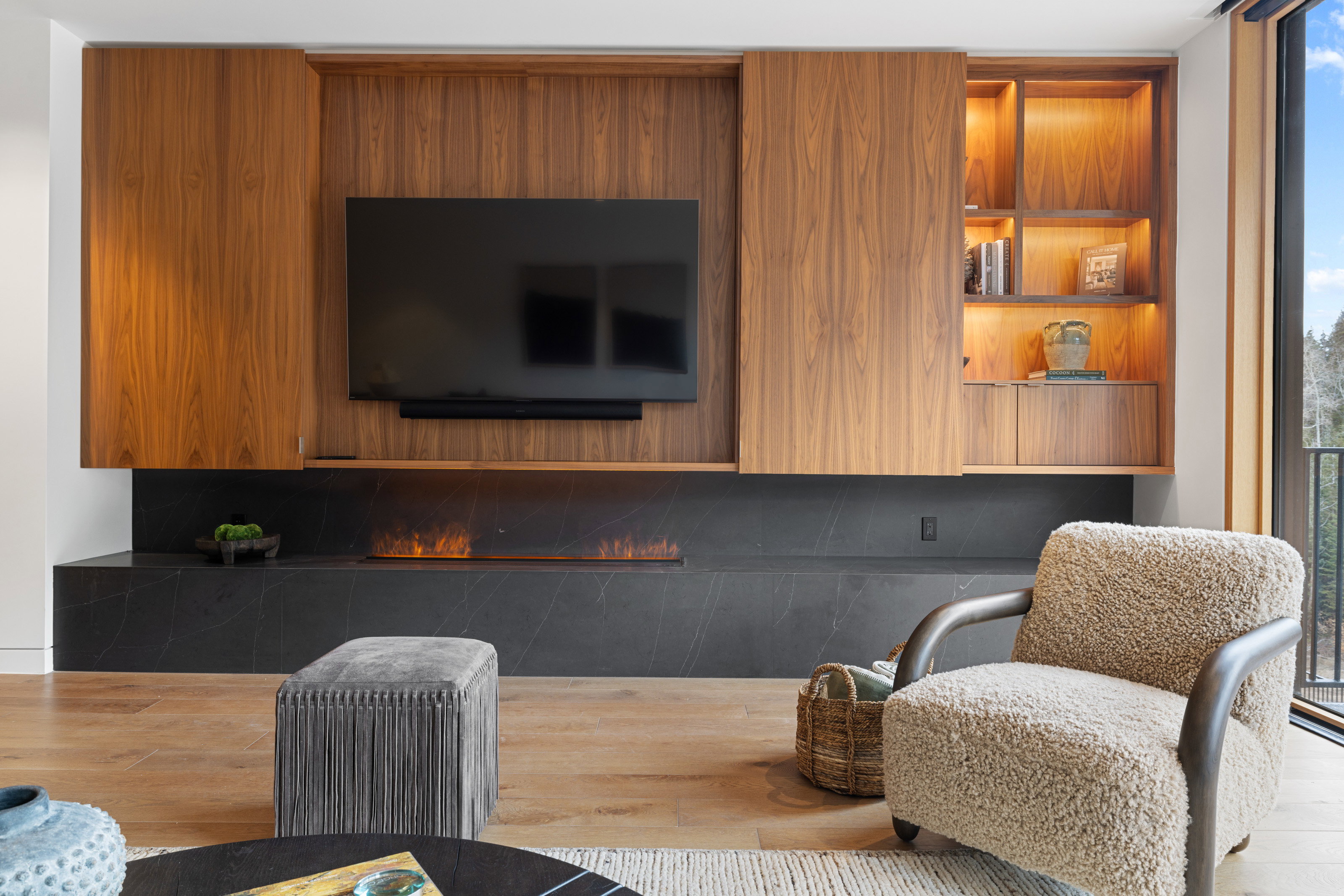 Custom built-in media center with wood-finish cabinetry, integrated shelving with accent lighting, a linear fireplace, and wood-finish flooring