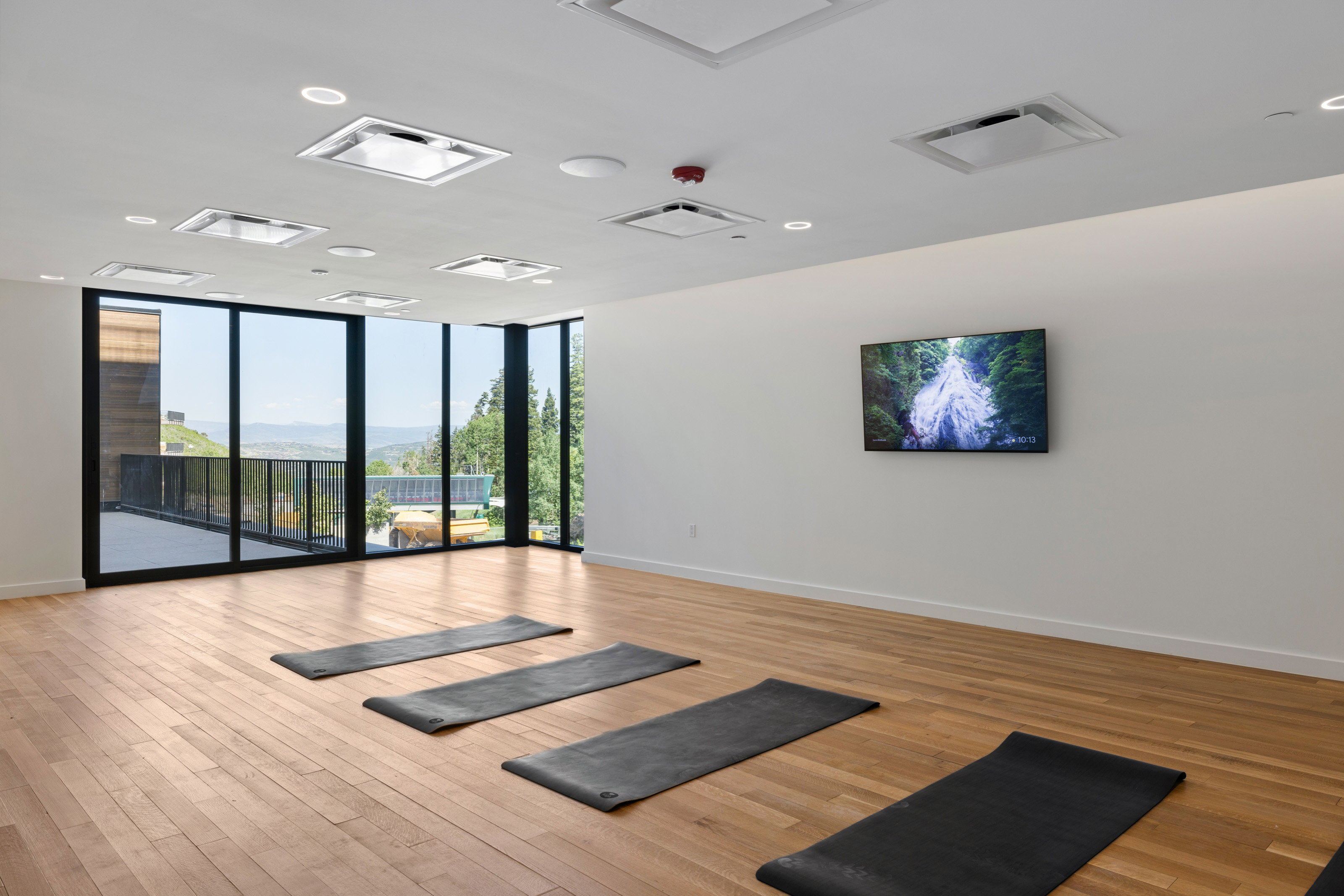 Spacious room featuring wood-finish flooring, floor-to-ceiling windows, multiple recessed ceiling lights, and a wall-mounted display