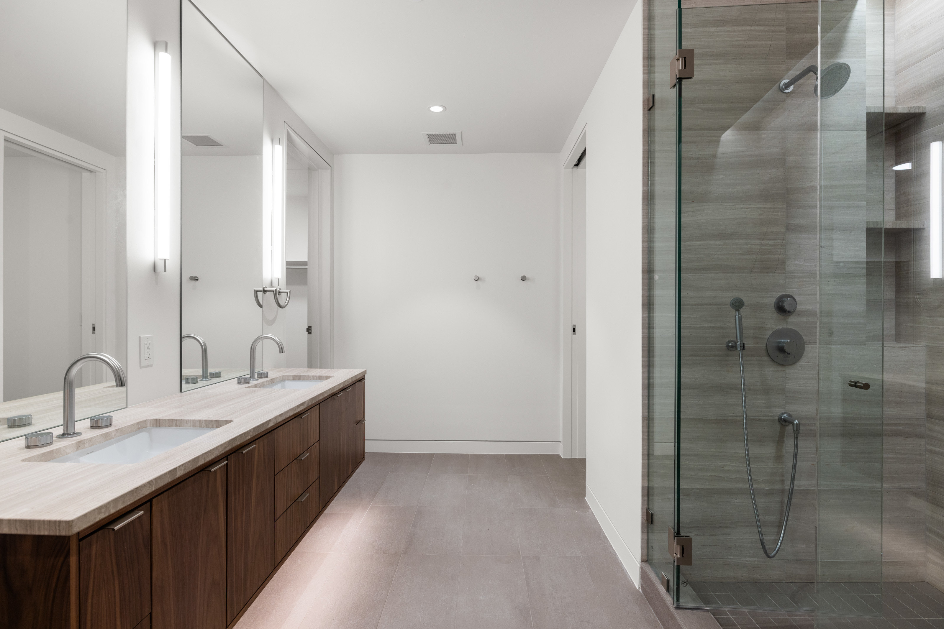 Modern bathroom featuring a dual vanity with a light-toned countertop, under-cabinet lighting, and a full-length mirror