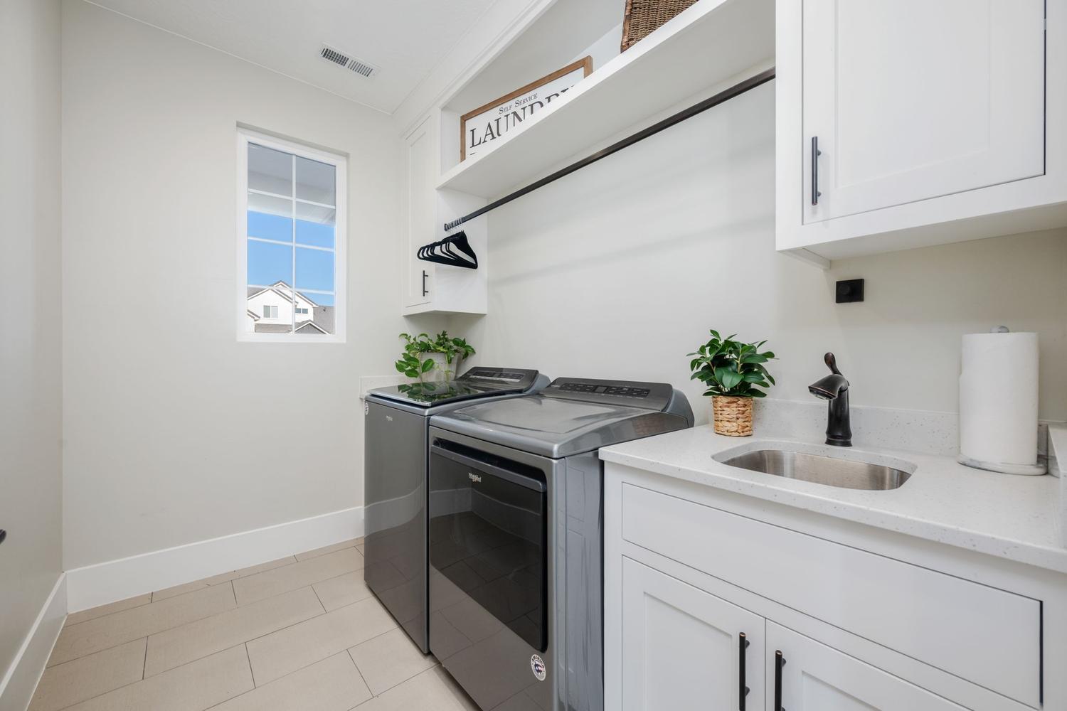 Dedicated laundry area featuring a utility sink with a black faucet, white cabinetry with black hardware, and ample counter space
