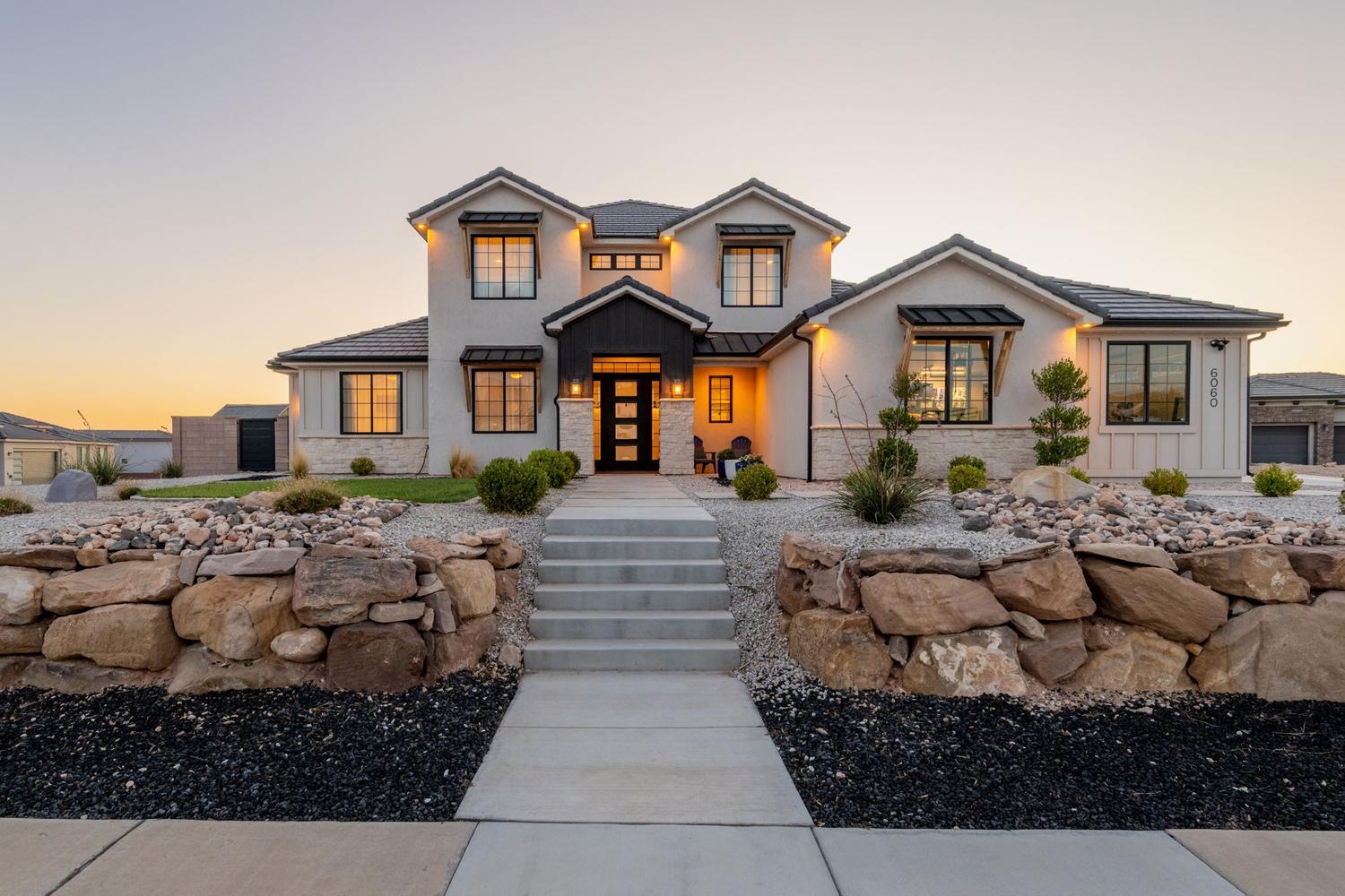 Contemporary two-story residence featuring a stucco and stone exterior, a dark tile roof, and prominent dormer windows