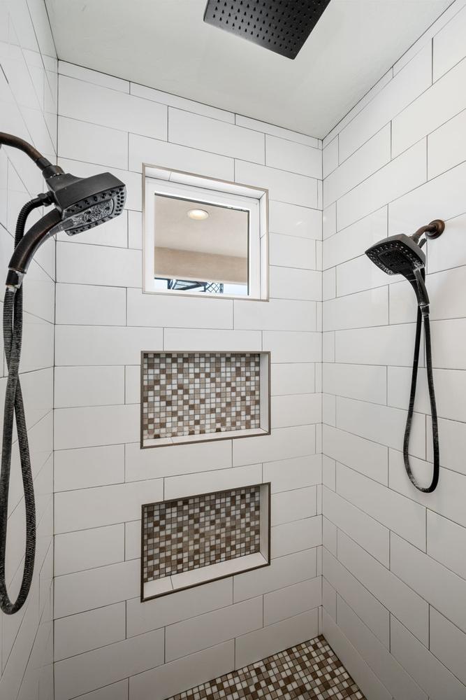 Shower featuring subway tile walls, two recessed niches with mosaic tile backing, a rain shower head, and a handheld shower fixture