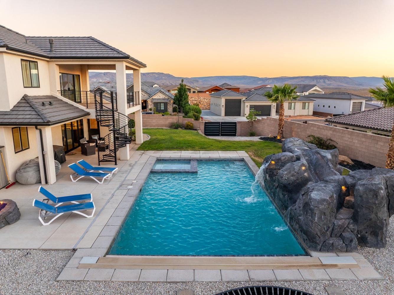 Resort-style backyard featuring a rectangular pool with an integrated spa, rock waterfall, and expansive paved patio