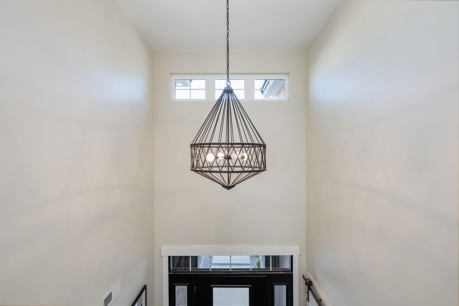 Two-story entryway featuring a geometric chandelier, transom windows, and a dark-paneled door with glass inserts