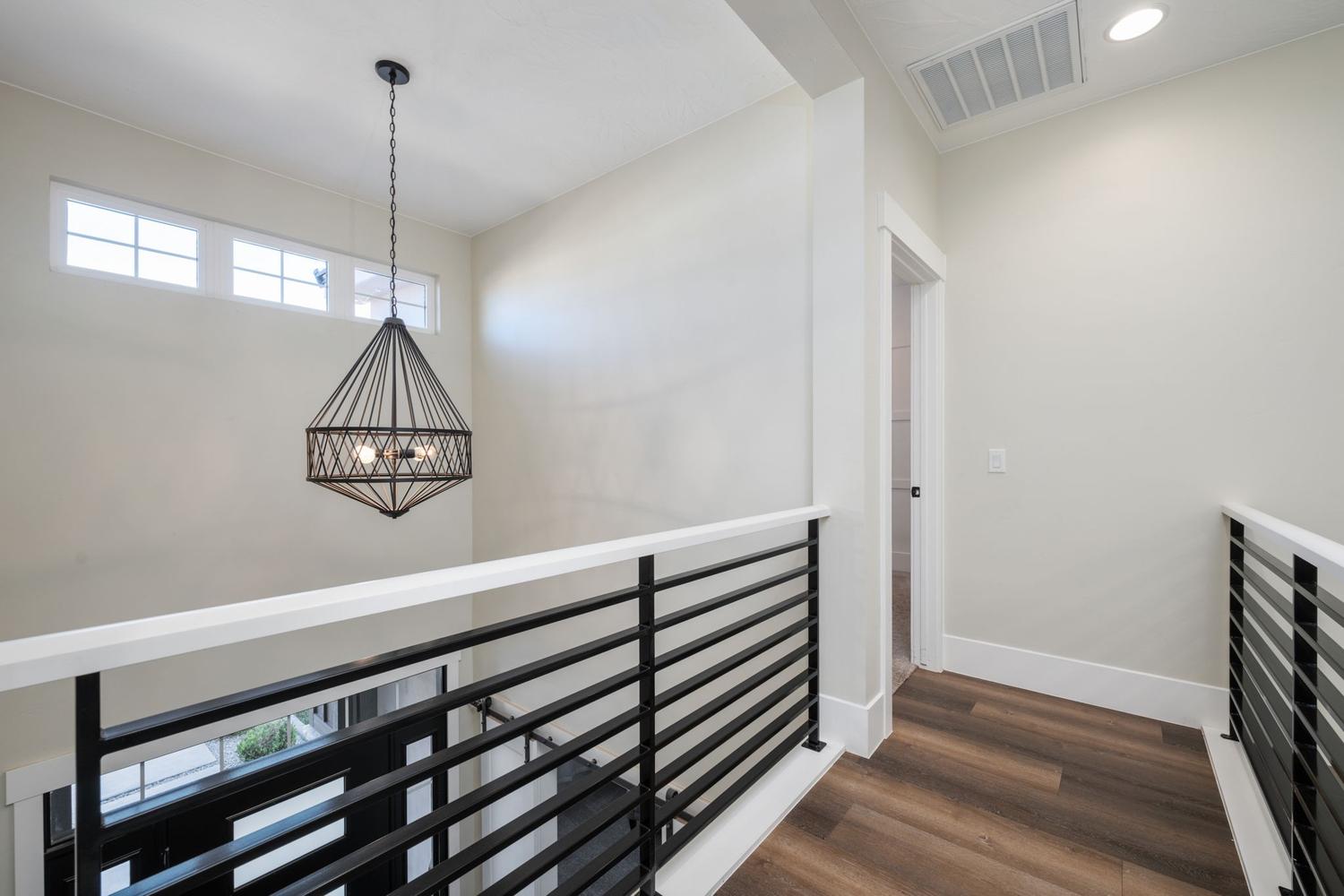 Upper-level hallway featuring wood-finish flooring, a contemporary black metal chandelier, and white walls with transom windows