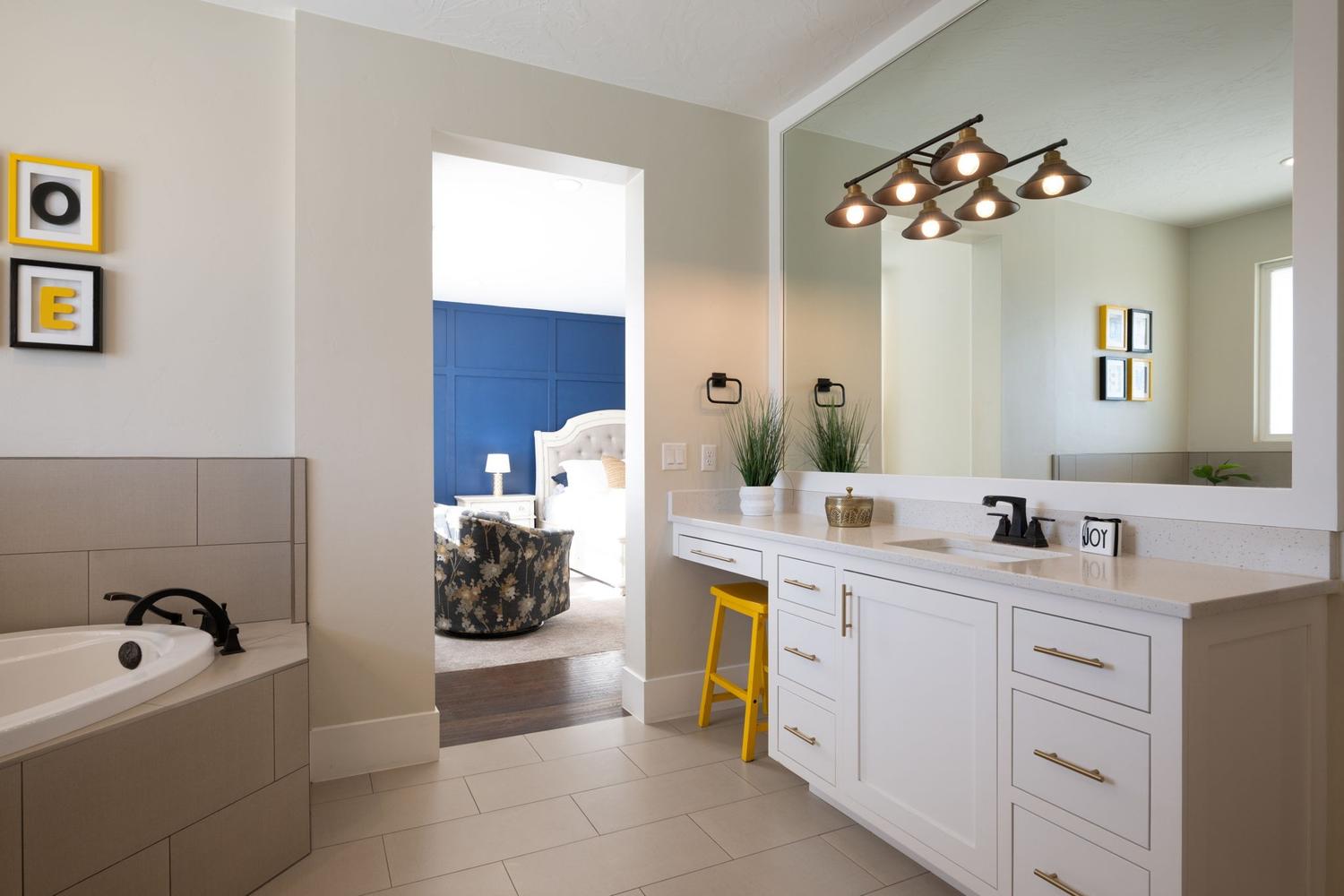 White vanity with a single undermount sink, a large wall mirror, and a bronze-finish light fixture