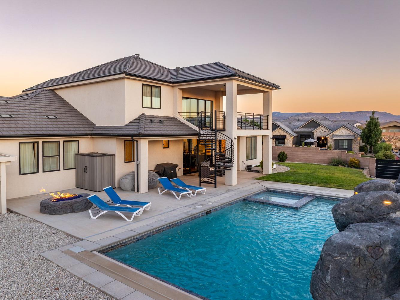 Outdoor living area featuring a swimming pool with integrated spa, a fire pit, and a spiral staircase leading to an upper-level balcony