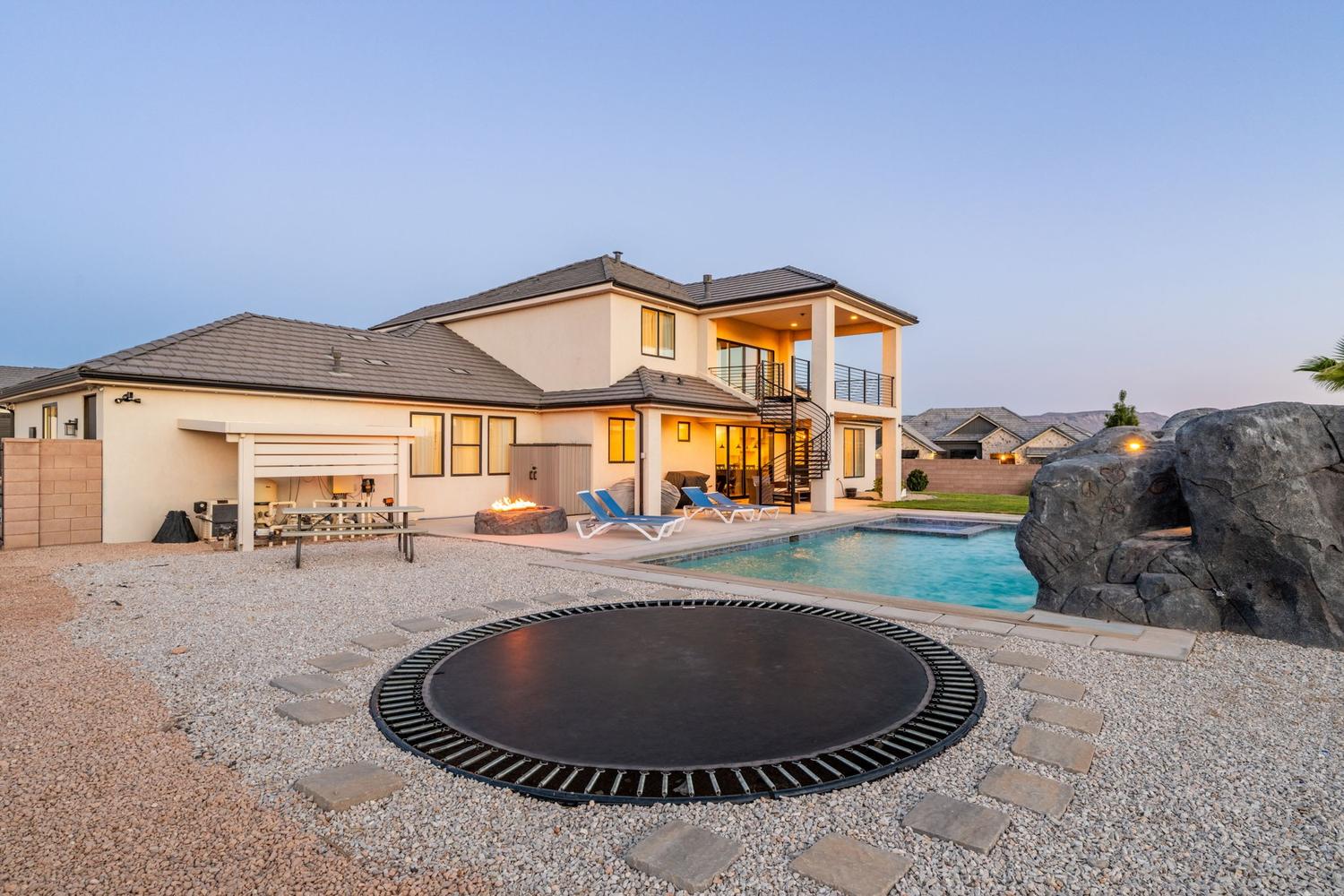 Spacious backyard featuring a rectangular swimming pool with integrated spa, a fire pit area, and a spiral staircase leading to a second-story balcony