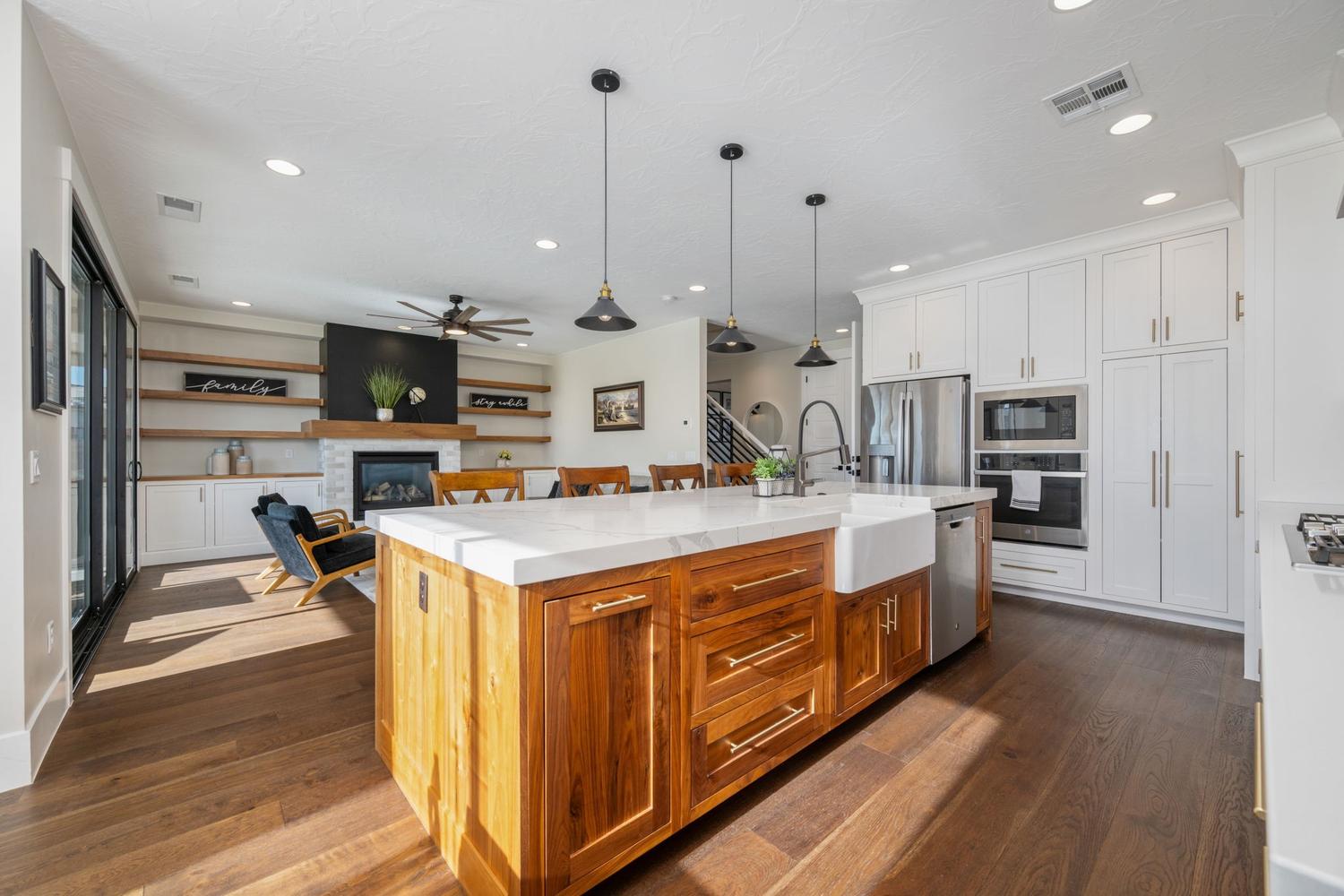 Open-concept living space featuring a central kitchen island with a farmhouse sink and wood-finish cabinetry, a full suite of stainless steel appliances, and wood-finish flooring
