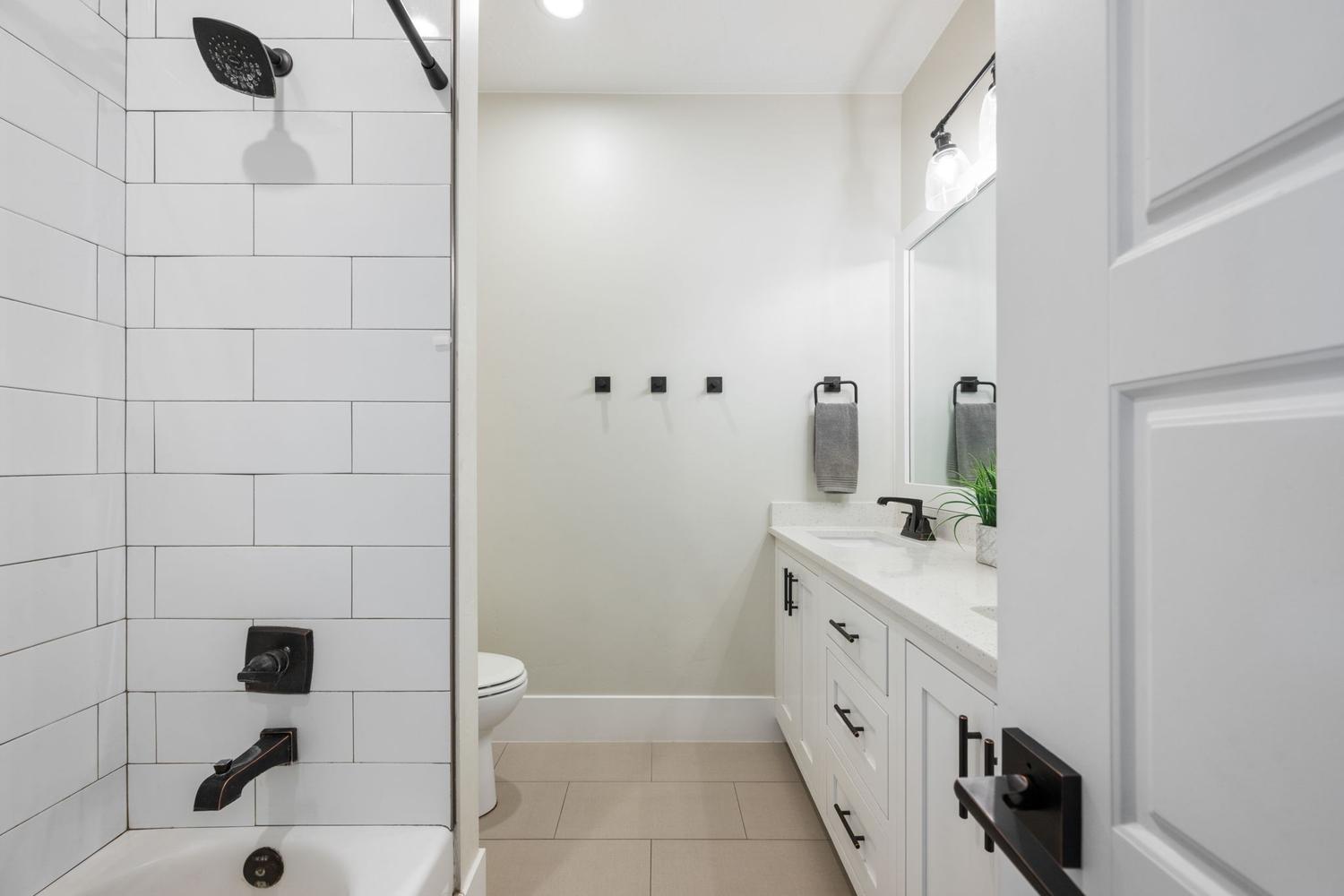 Modern bathroom featuring a white subway tile shower surround with matte black fixtures, a white panel vanity with a light-colored countertop, and a contemporary vanity light fixture