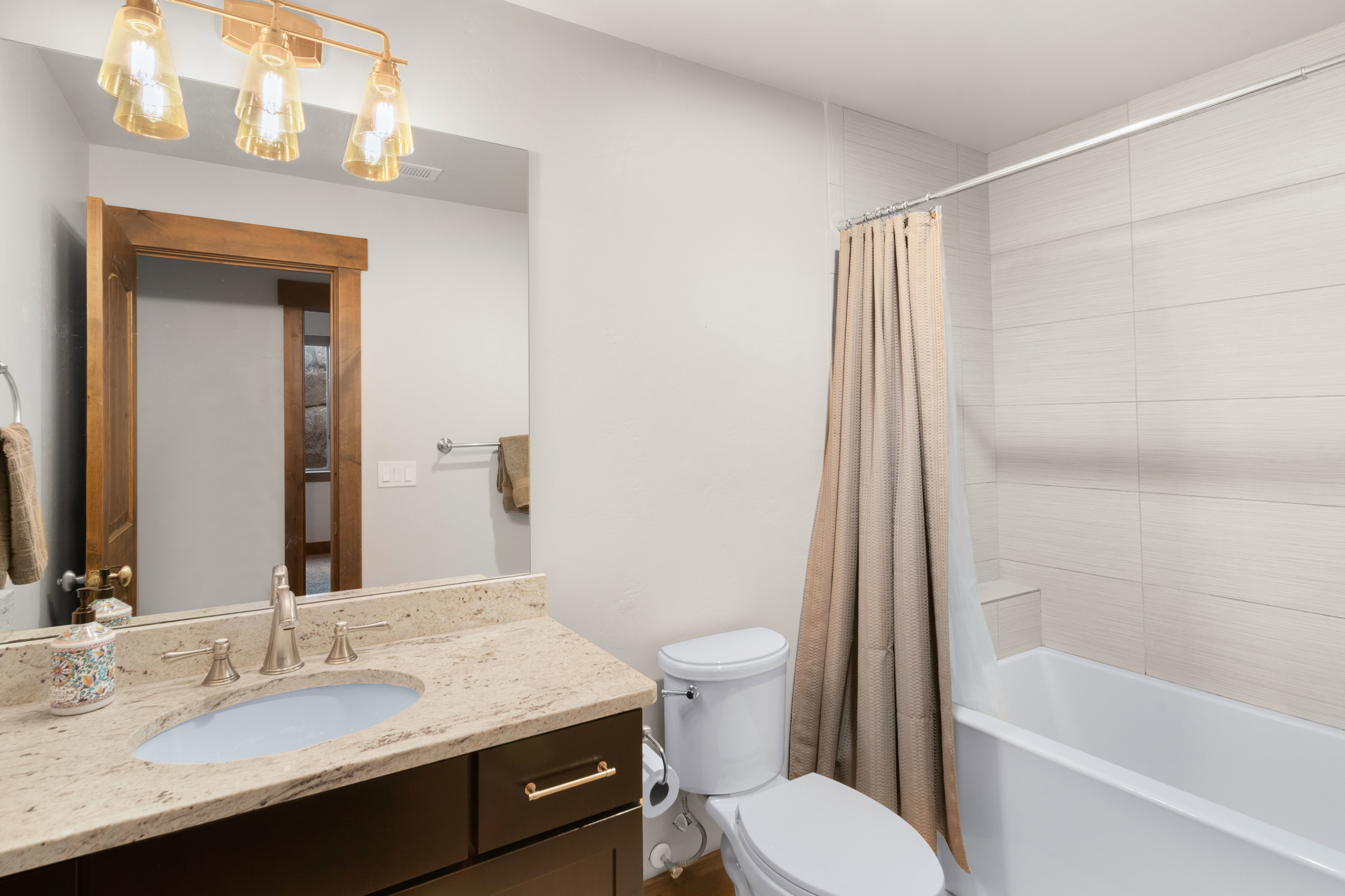Bathroom featuring a vanity with an oval undermount sink, a light-toned countertop, and a dark wood-finish cabinet with gold-tone hardware