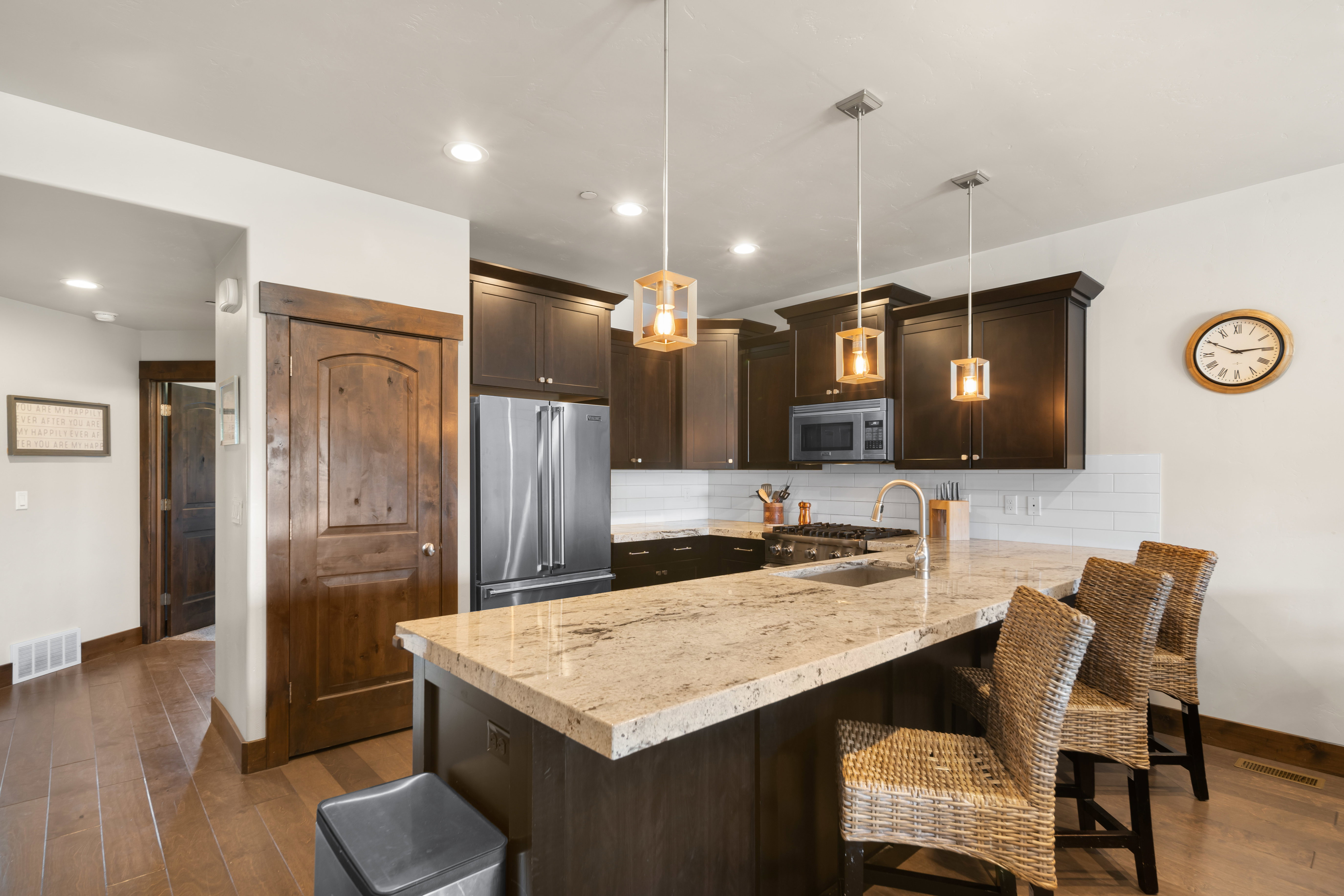Kitchen featuring an island with stone countertops, dark wood cabinetry, stainless steel appliances, a white subway tile backsplash, and wood-finish flooring