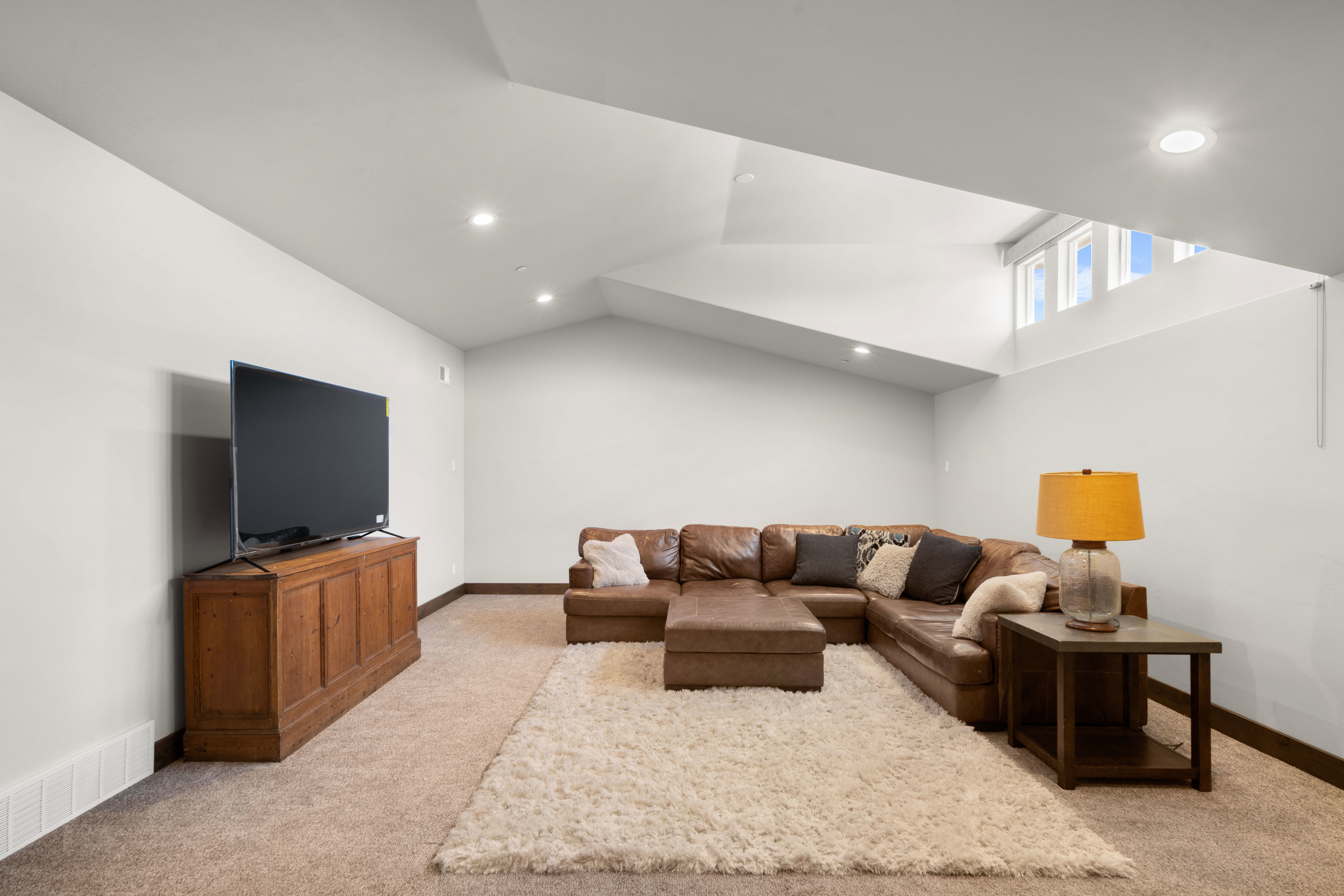 Spacious living area featuring neutral carpeting, recessed lighting, white walls, wood-finish baseboards, and high windows providing natural light