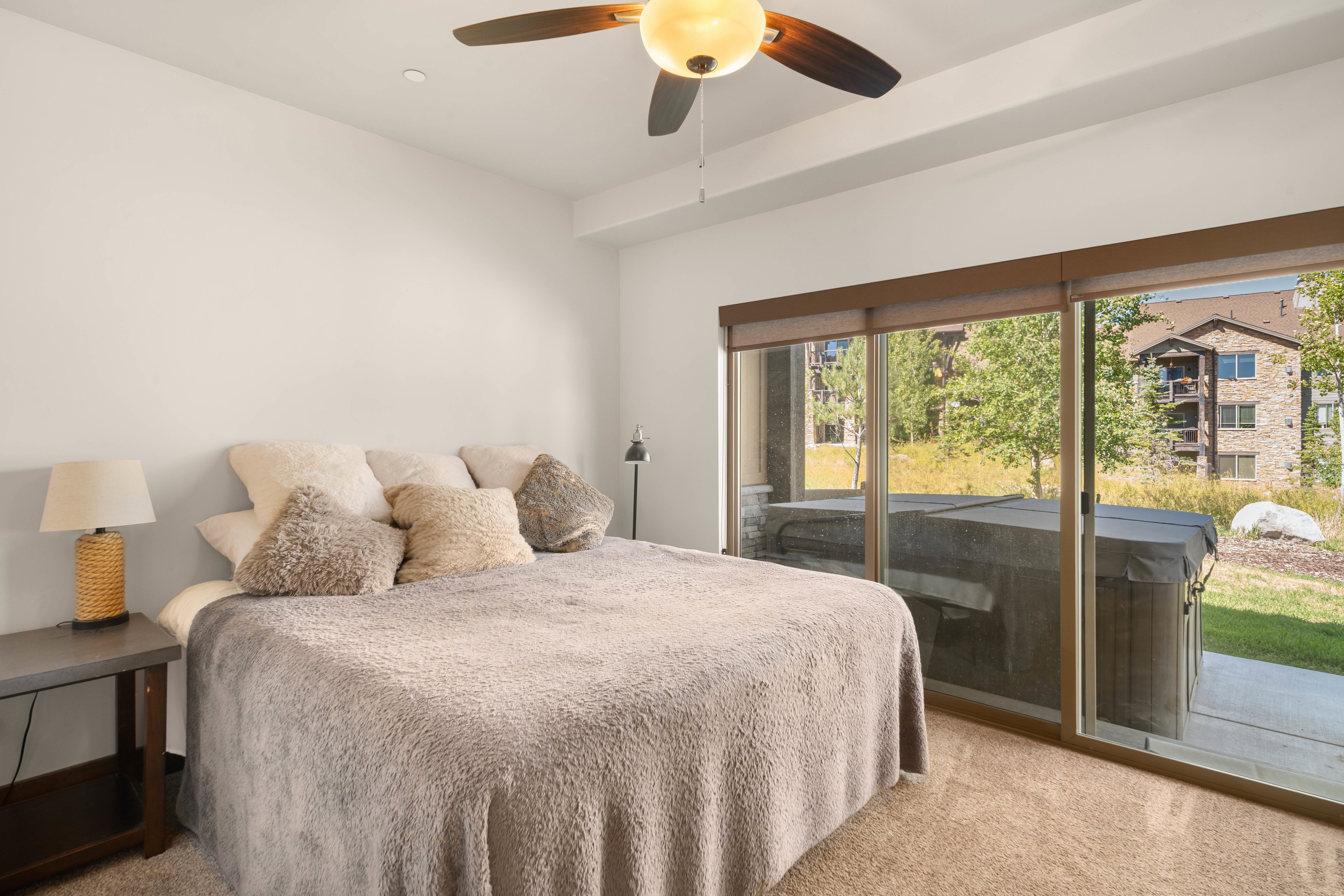 Carpeted room featuring a ceiling fan with integrated lighting, a sliding glass door providing outdoor access, and a private hot tub on a concrete patio