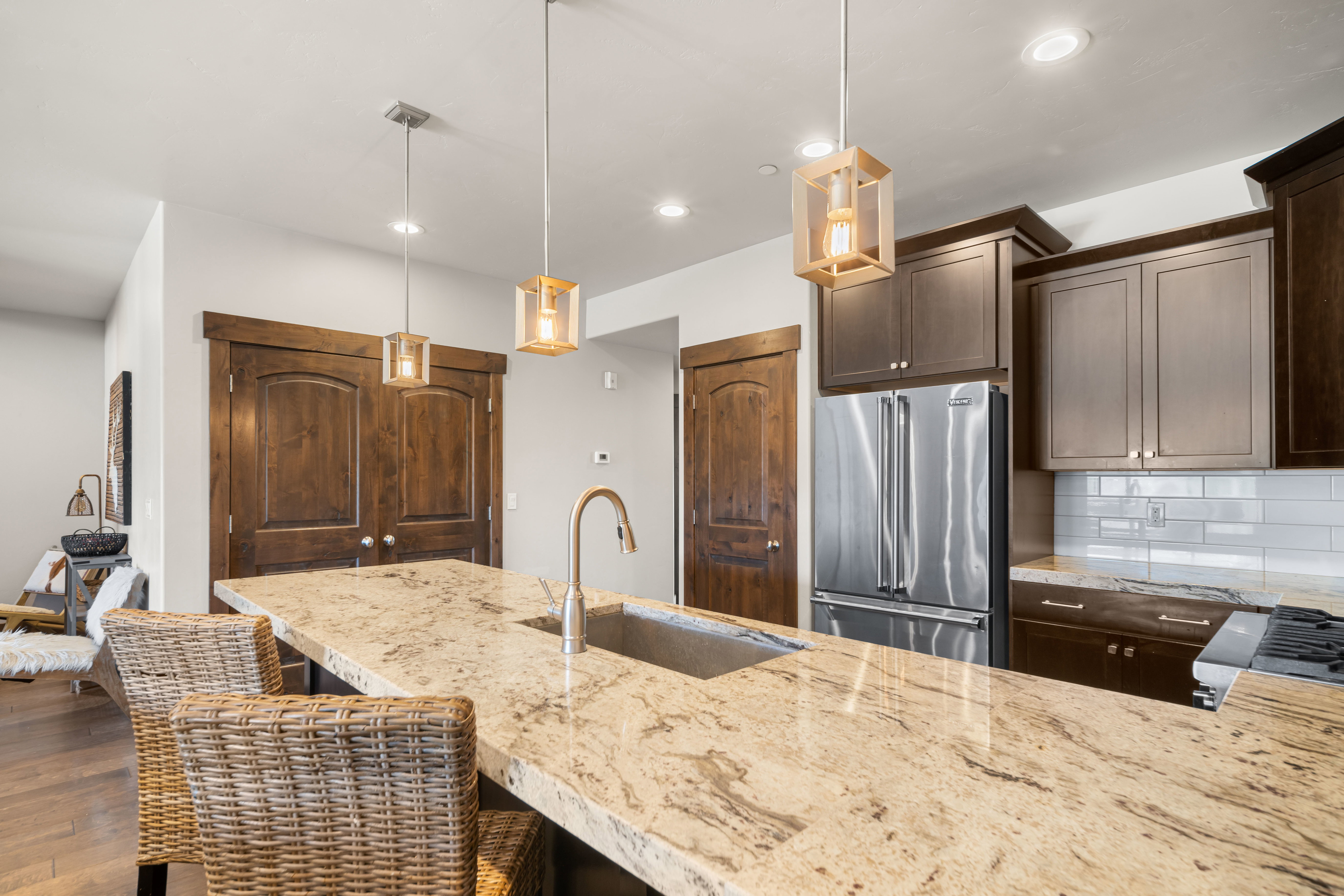 Kitchen island featuring a single-basin sink with a gooseneck faucet, light-toned granite countertop, and three pendant light fixtures
