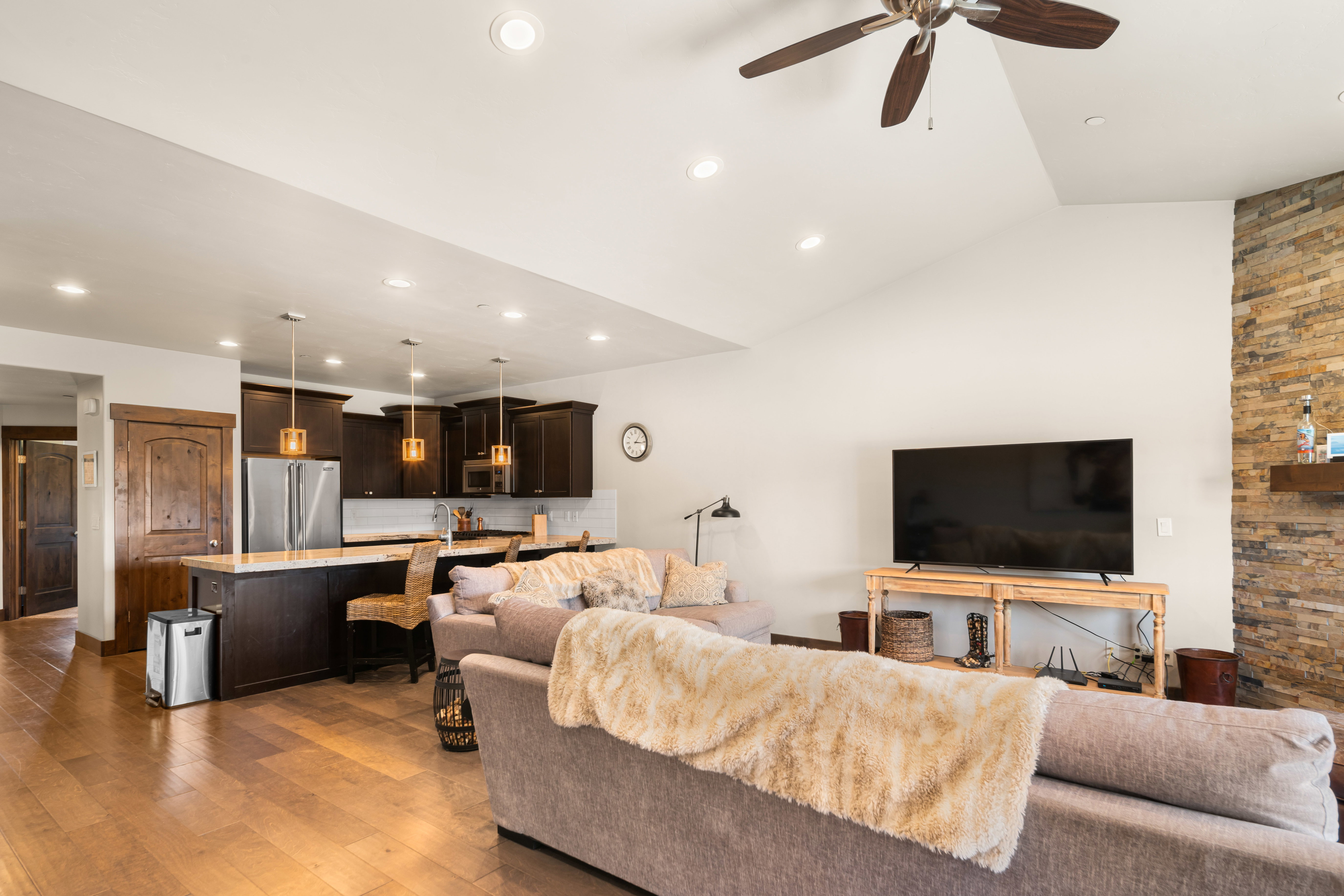 Open-concept living area featuring wood-finish flooring, vaulted ceilings, and a stacked stone accent wall