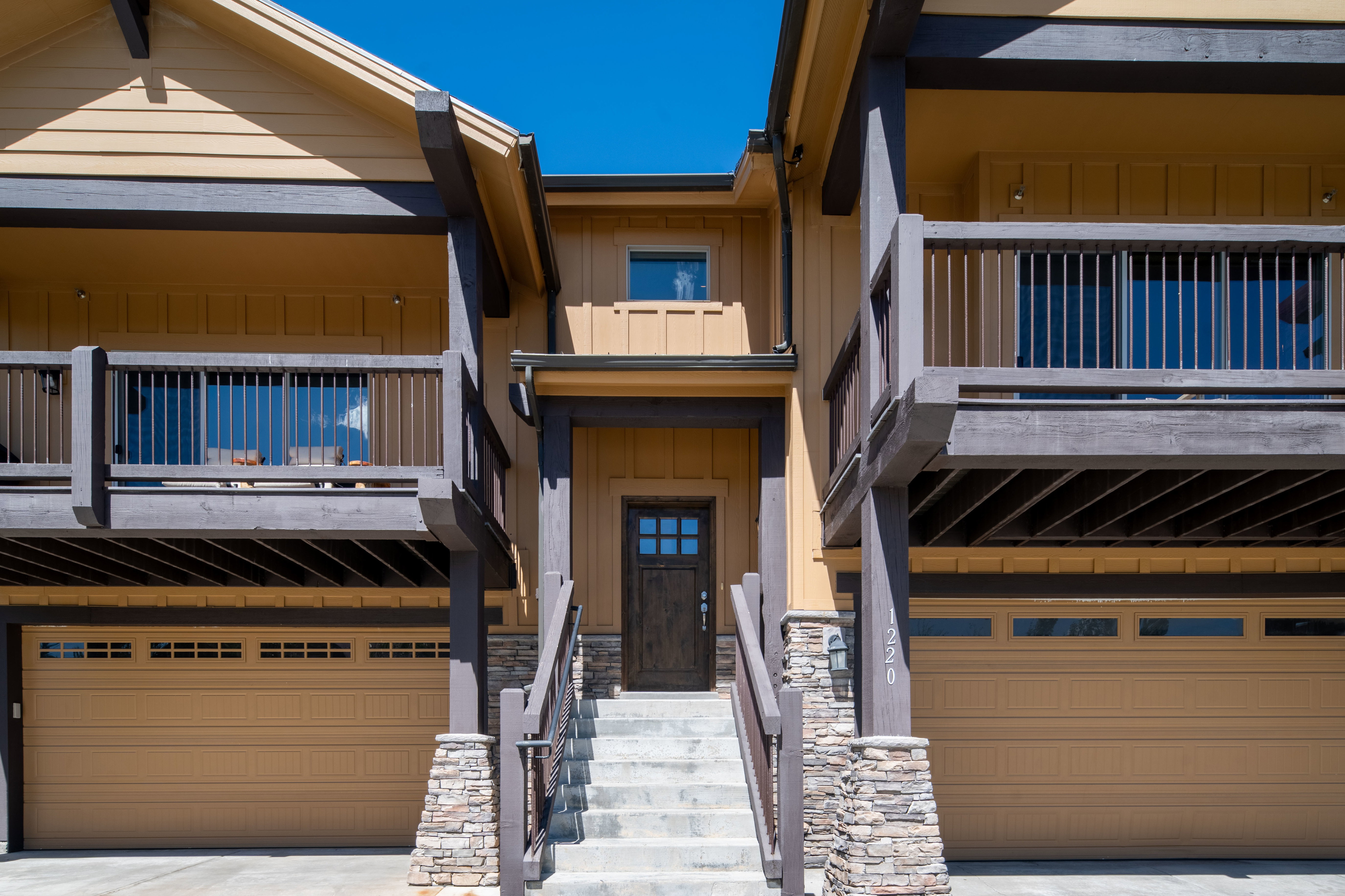 Multi-level exterior featuring a central entry with stone columns and wood-finish railings