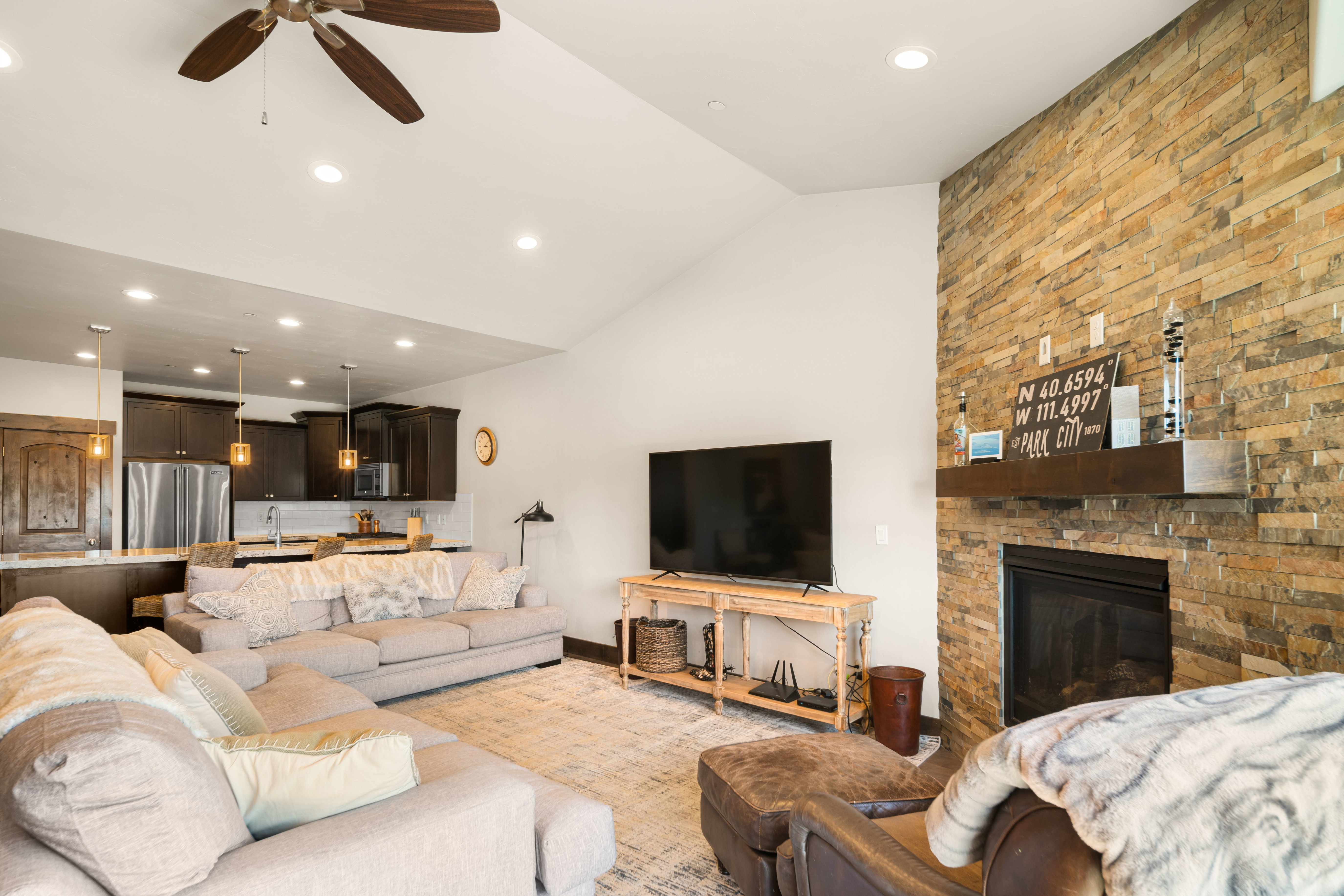Spacious living area featuring a stacked stone fireplace with a wood mantle, vaulted ceilings, and recessed lighting