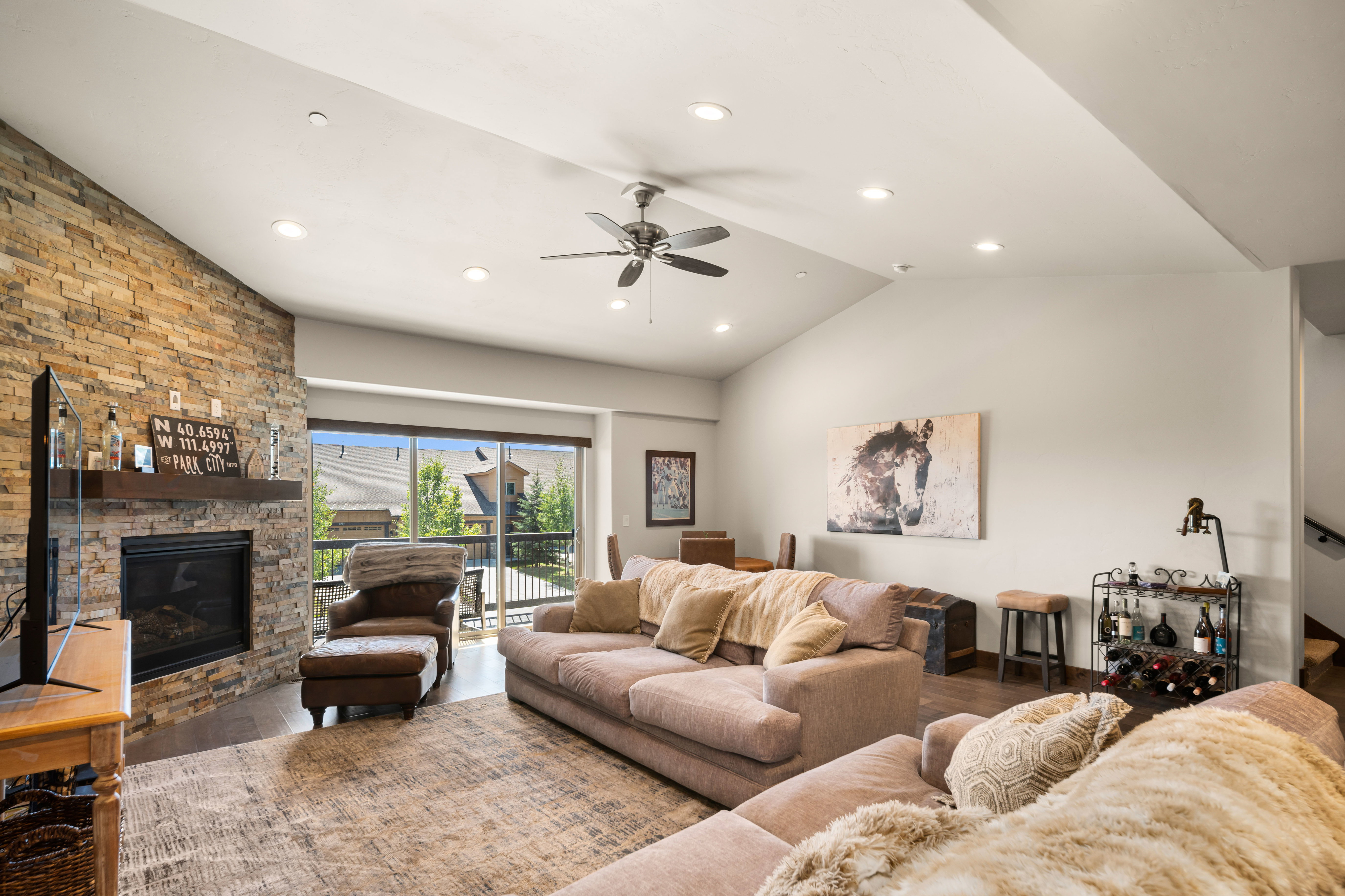 Spacious living area featuring a stone-clad fireplace with a wood mantle, vaulted ceilings, recessed lighting, and wood-finish flooring