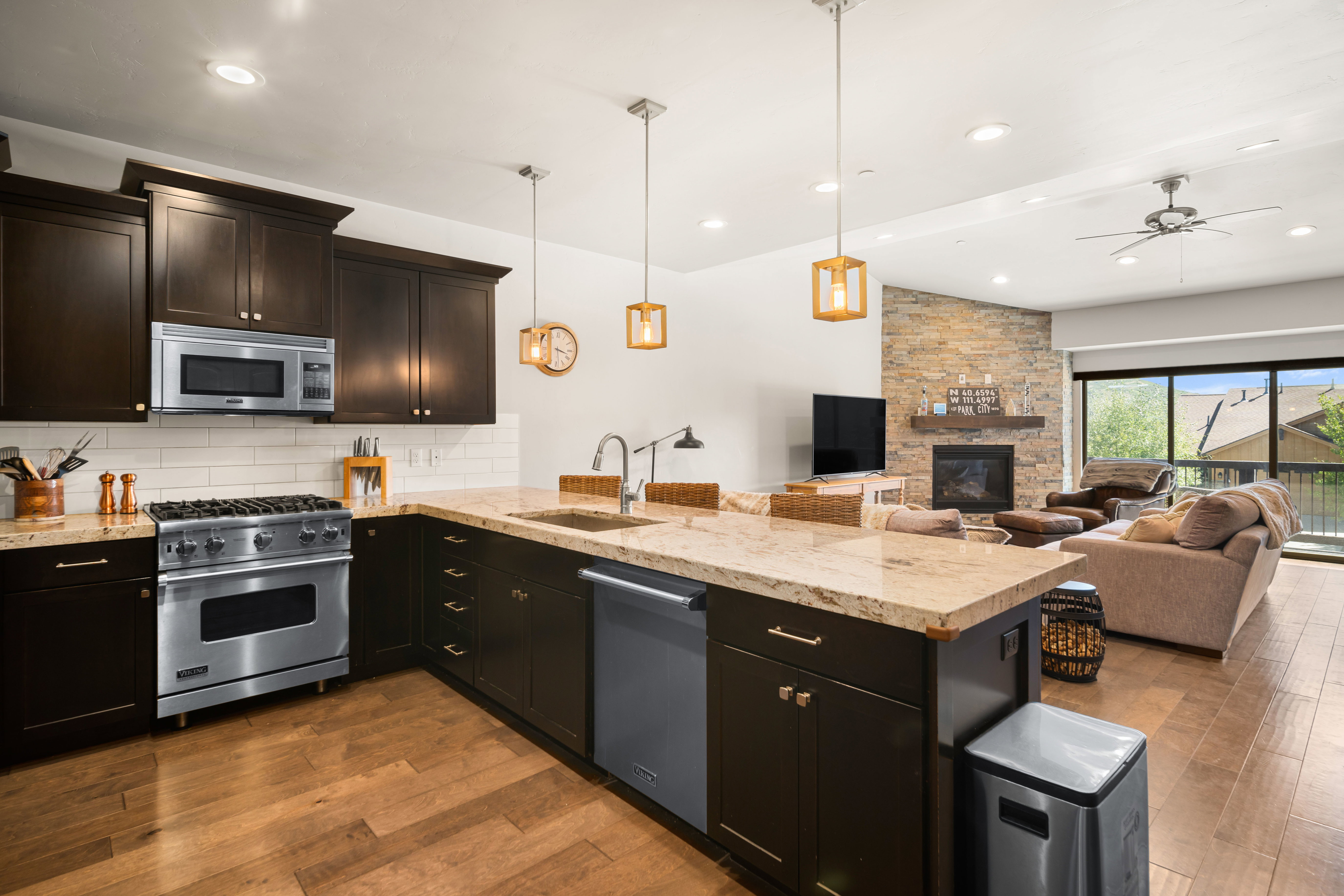 Gourmet kitchen with dark wood cabinetry, stainless steel appliances, and light-toned countertops, featuring a large island with integrated sink