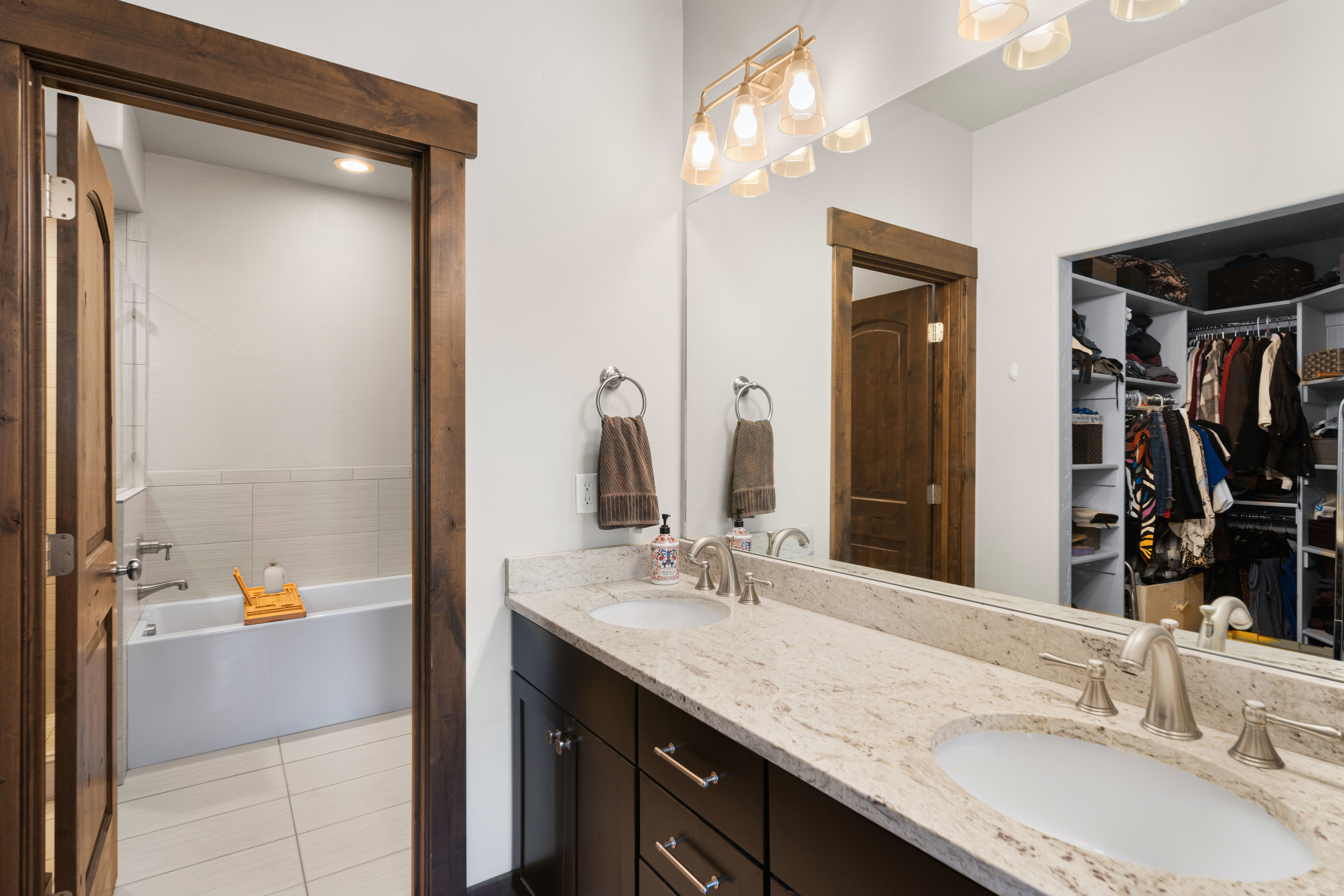Bathroom vanity featuring dual under-mount sinks, a light-toned stone countertop, and dark wood-finish cabinetry
