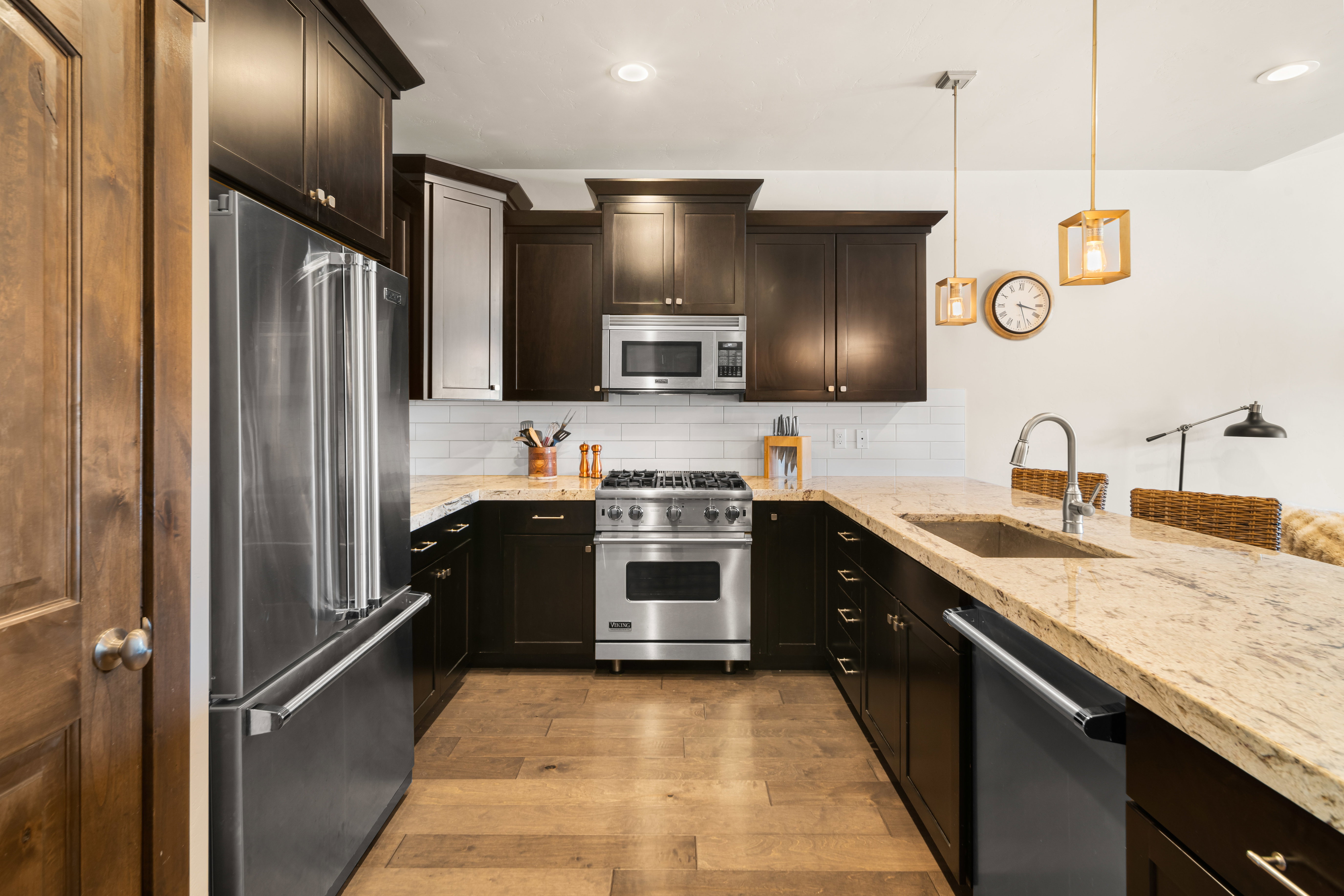 Gourmet kitchen featuring dark wood cabinetry, light granite countertops, stainless steel appliances, a subway tile backsplash, and wood-finish flooring