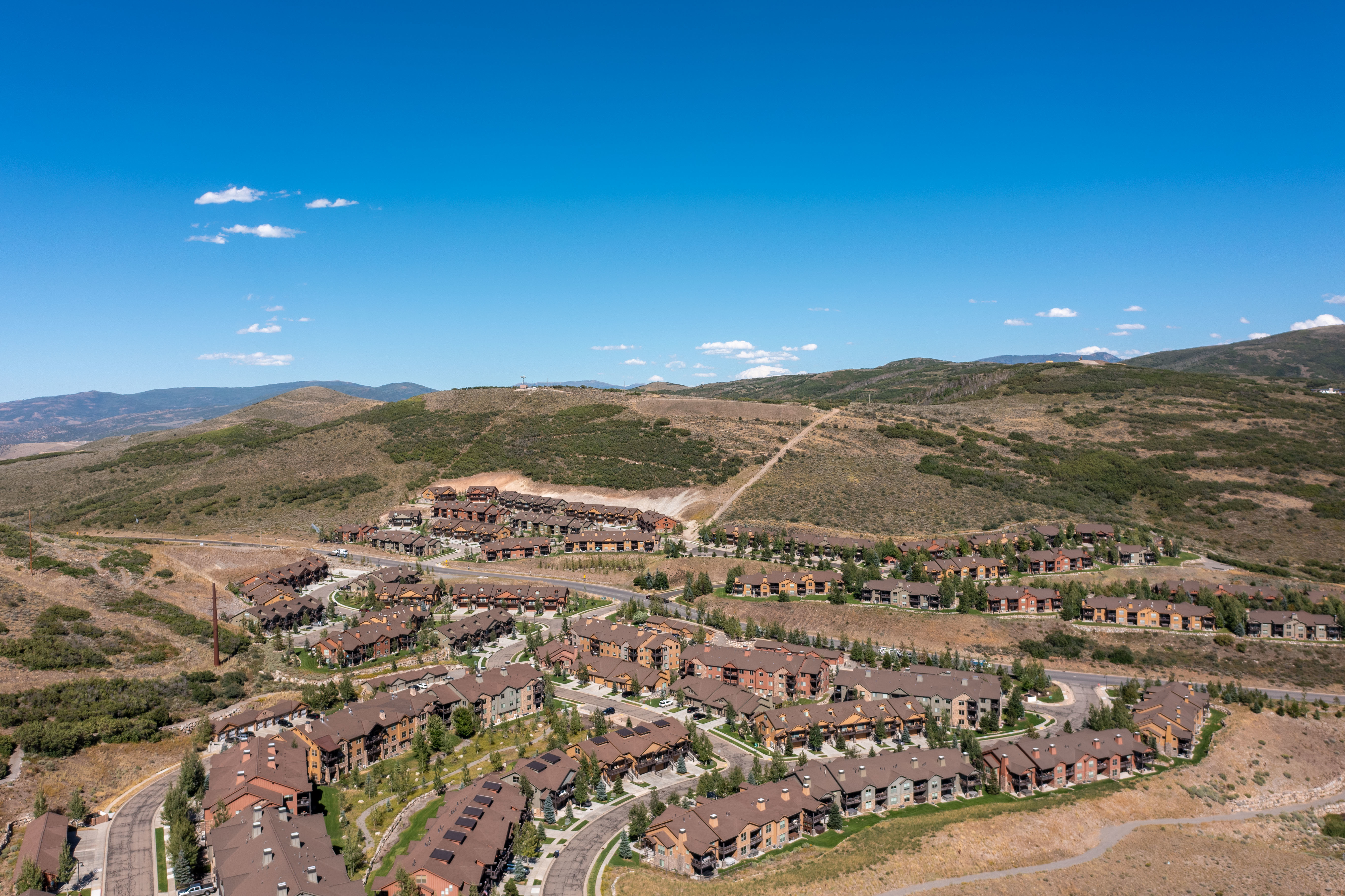 Expansive development featuring numerous multi-story residential buildings with brown roofs, nestled into a mountainous landscape