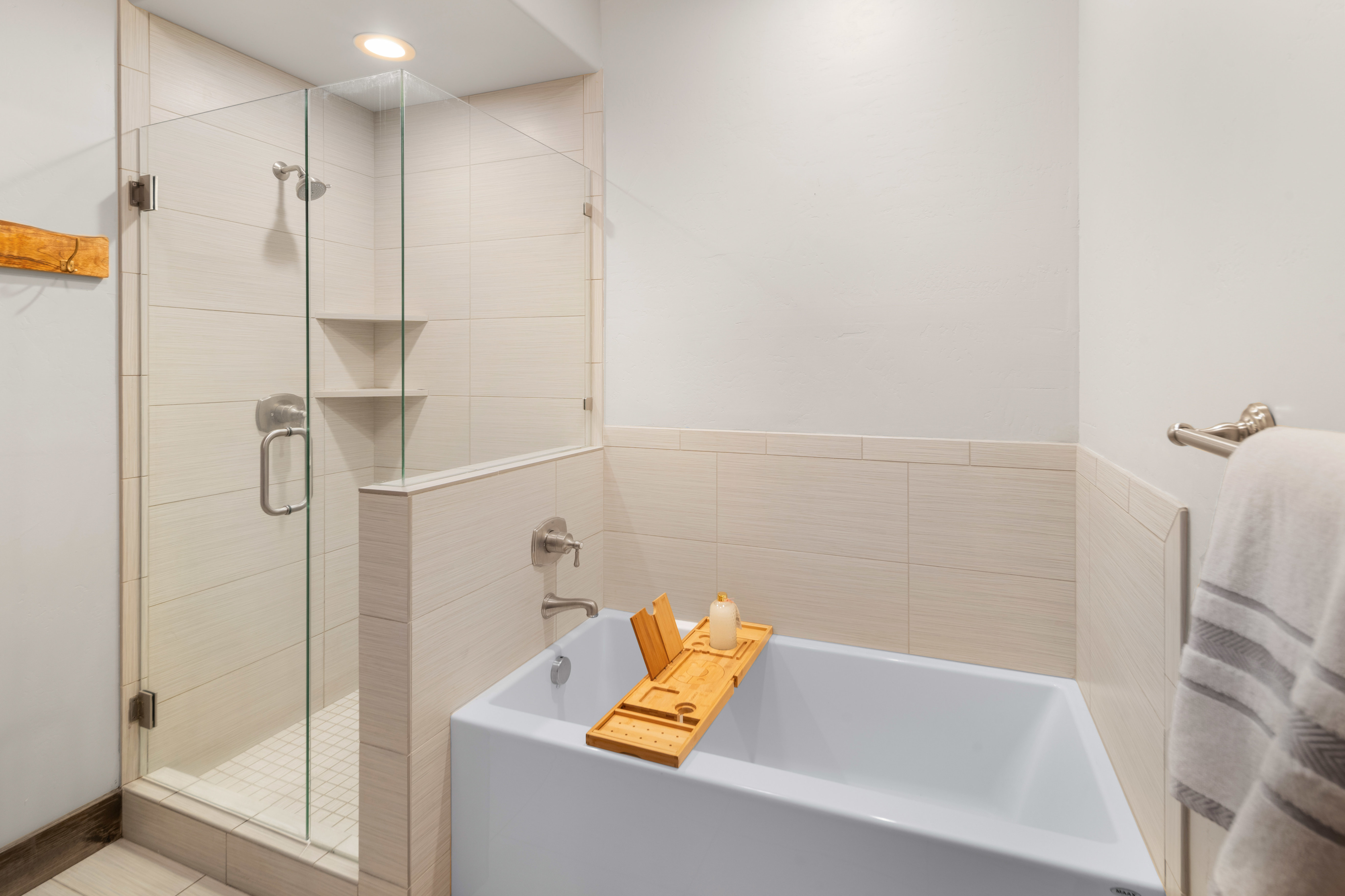 Bathroom featuring a glass-enclosed shower with integrated shelving, a built-in tub, and wall-mounted plumbing fixtures, all surrounded by light-toned wall tile