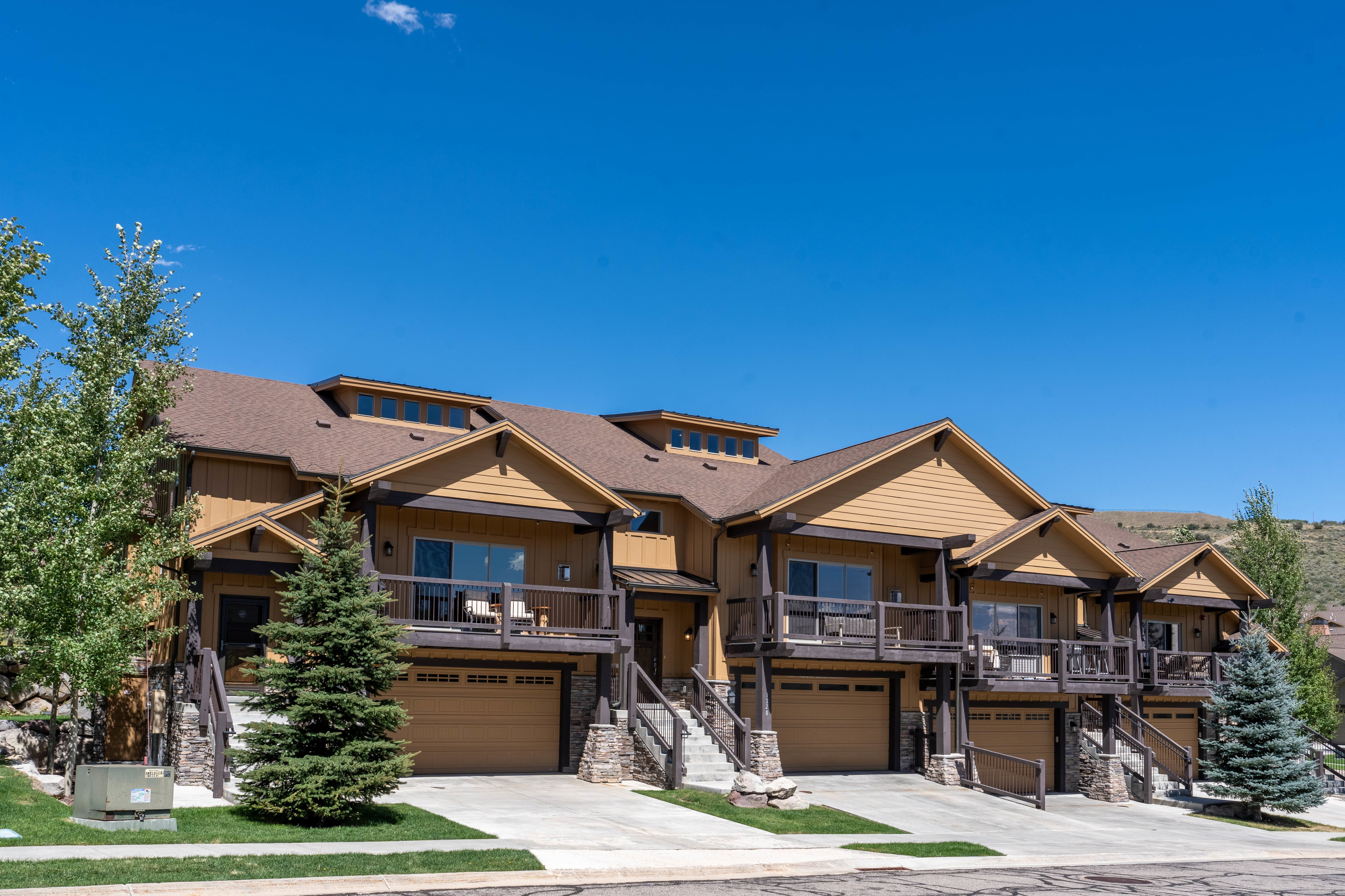 Multi-level townhome exteriors featuring wood siding with stone accents, individual attached garages, and private balconies
