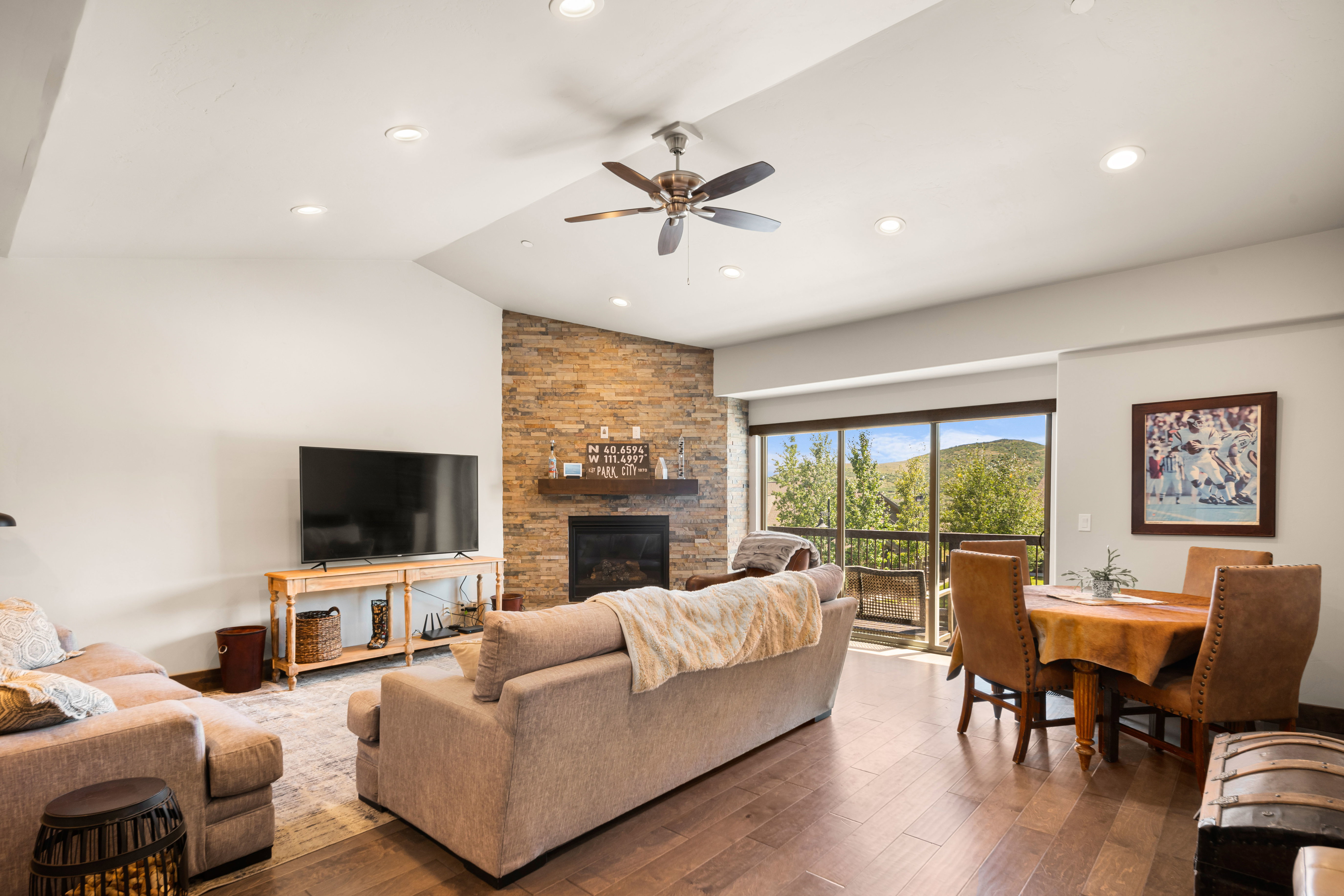 Open-concept living space featuring wood-finish flooring, a stone accent wall with a fireplace, and vaulted ceilings with recessed lighting