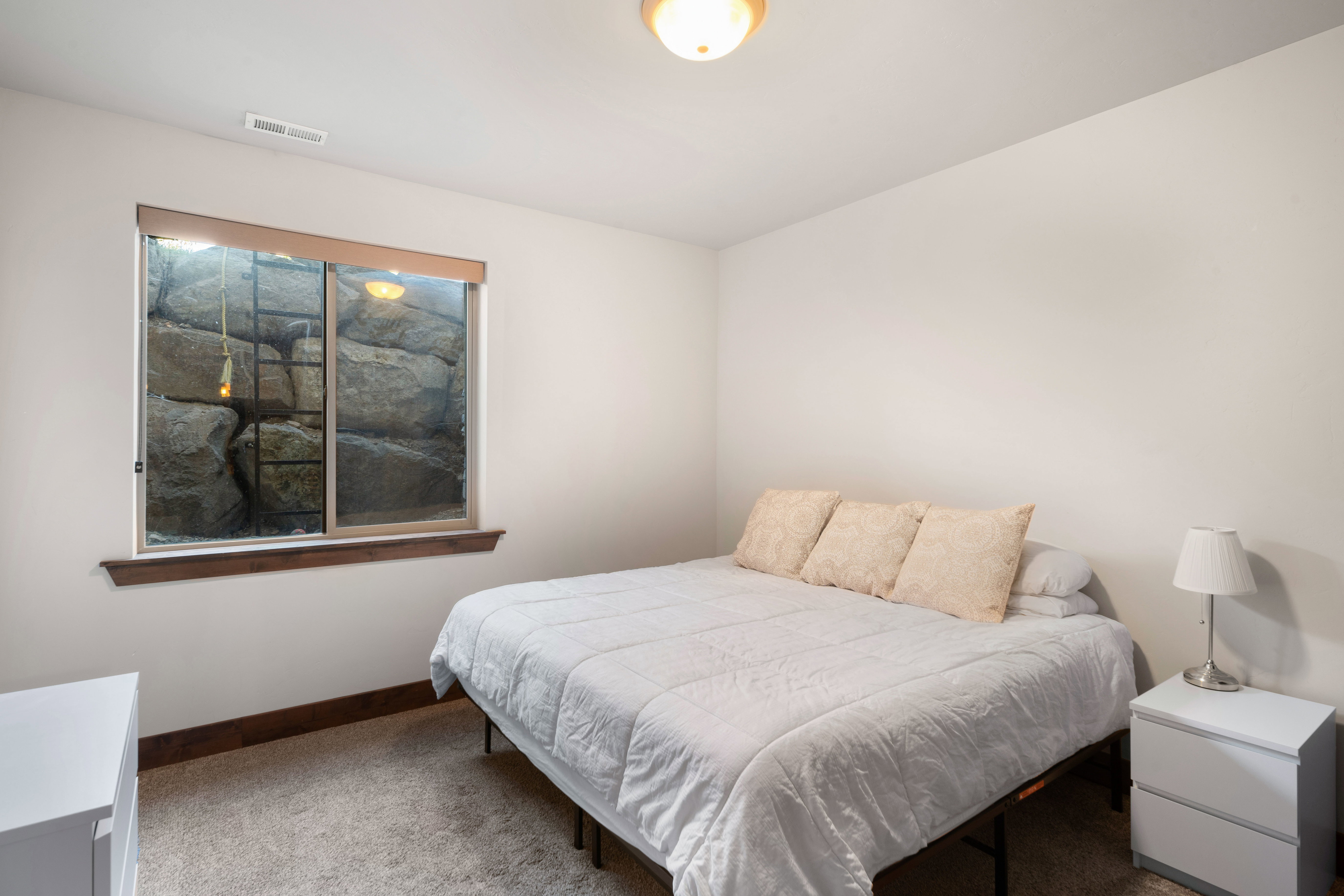 Bedroom featuring a textured carpet, white walls, and a recessed window with rock-effect well