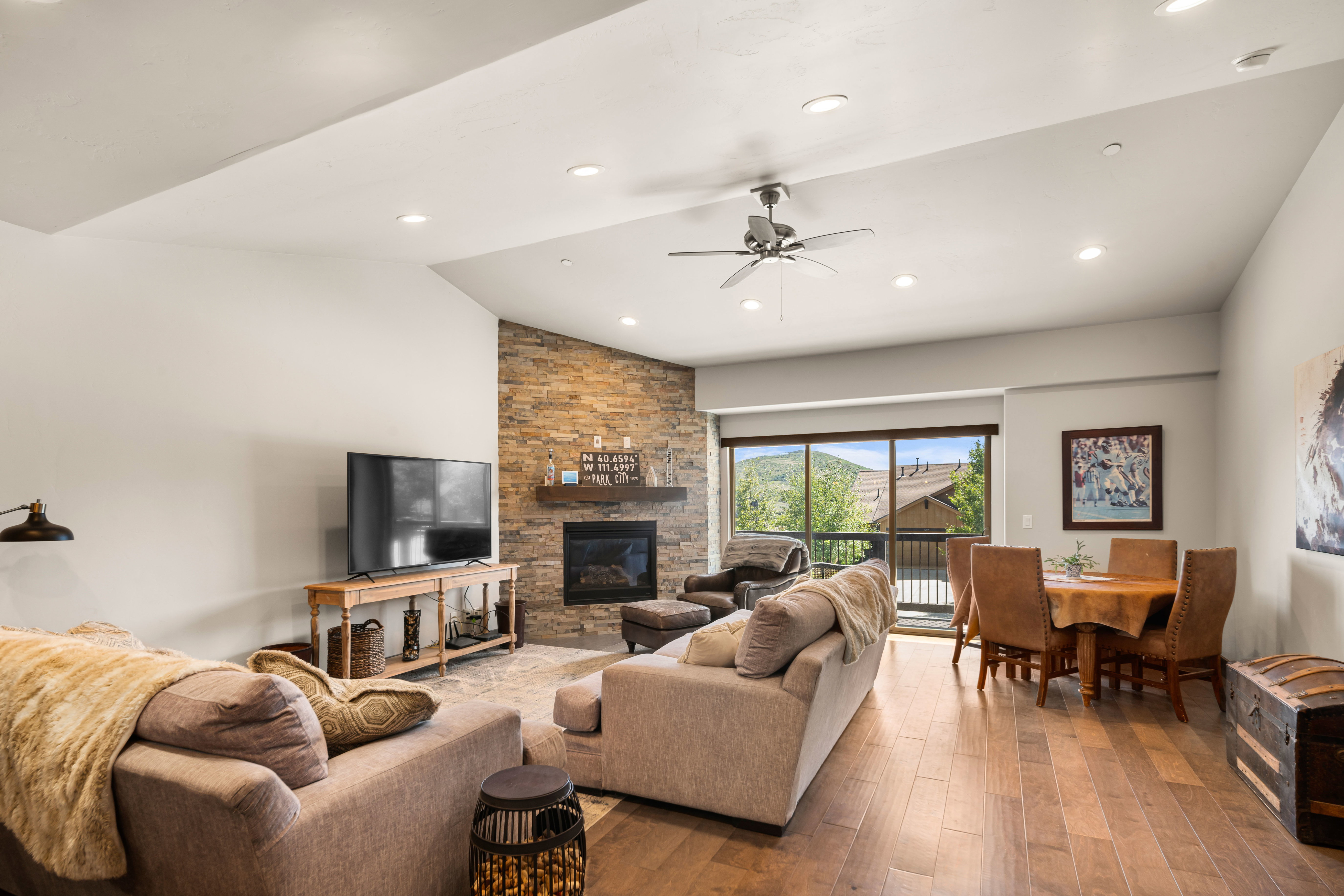 Open-concept living area with wood-finish flooring, a stone-clad fireplace, and a vaulted ceiling