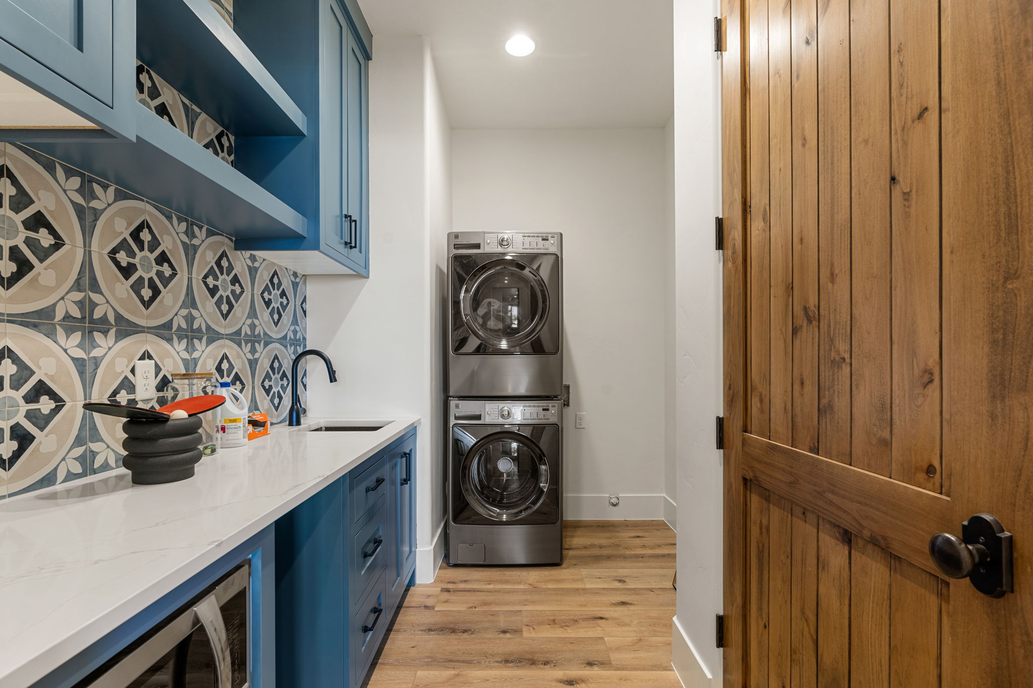 Laundry area featuring custom blue cabinetry with open shelving, a white countertop, patterned tile backsplash, and a matte black faucet