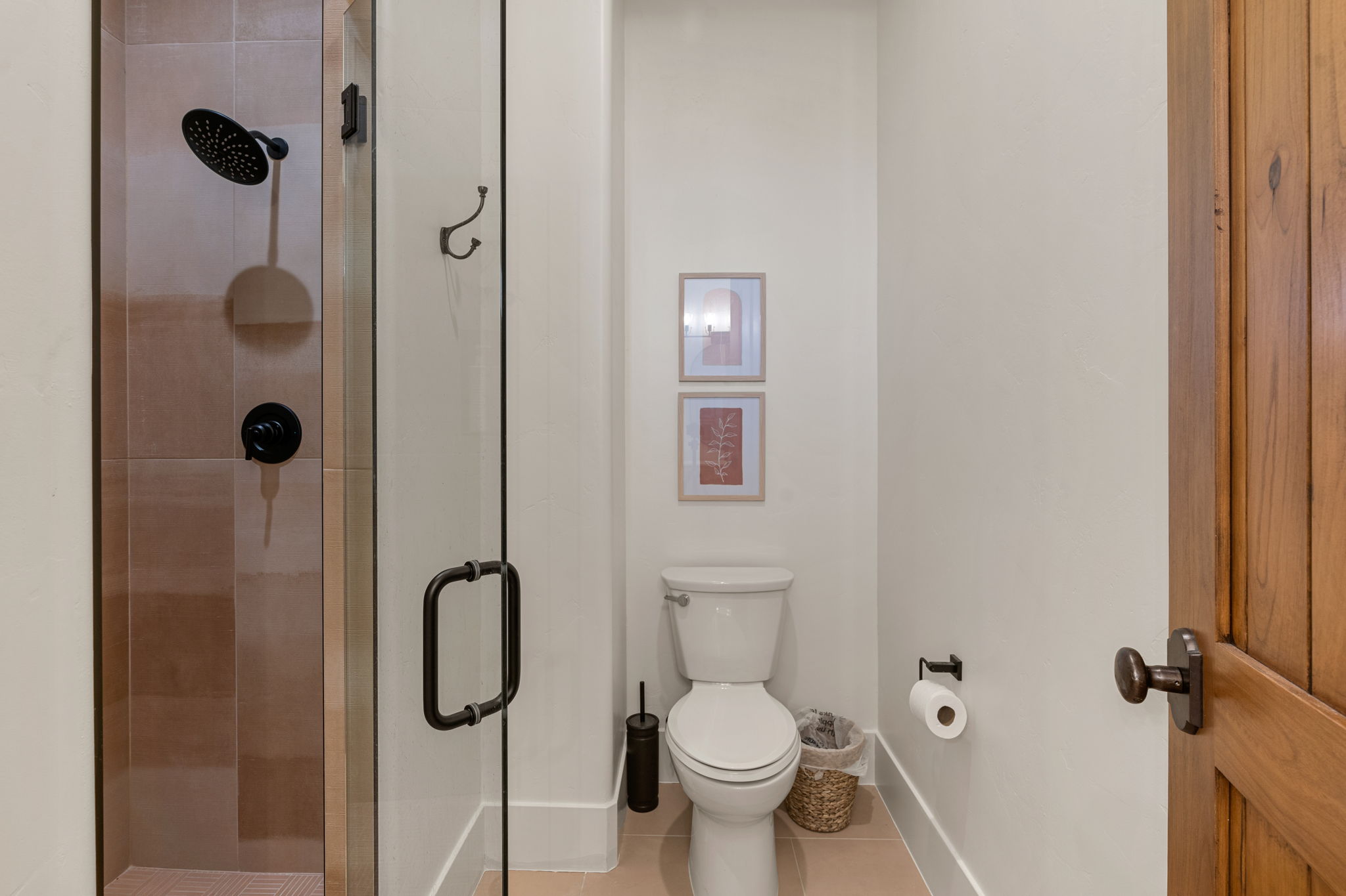 Contemporary bathroom featuring a frameless glass shower enclosure, matte black shower fixtures, a white toilet, and a solid wood paneled door