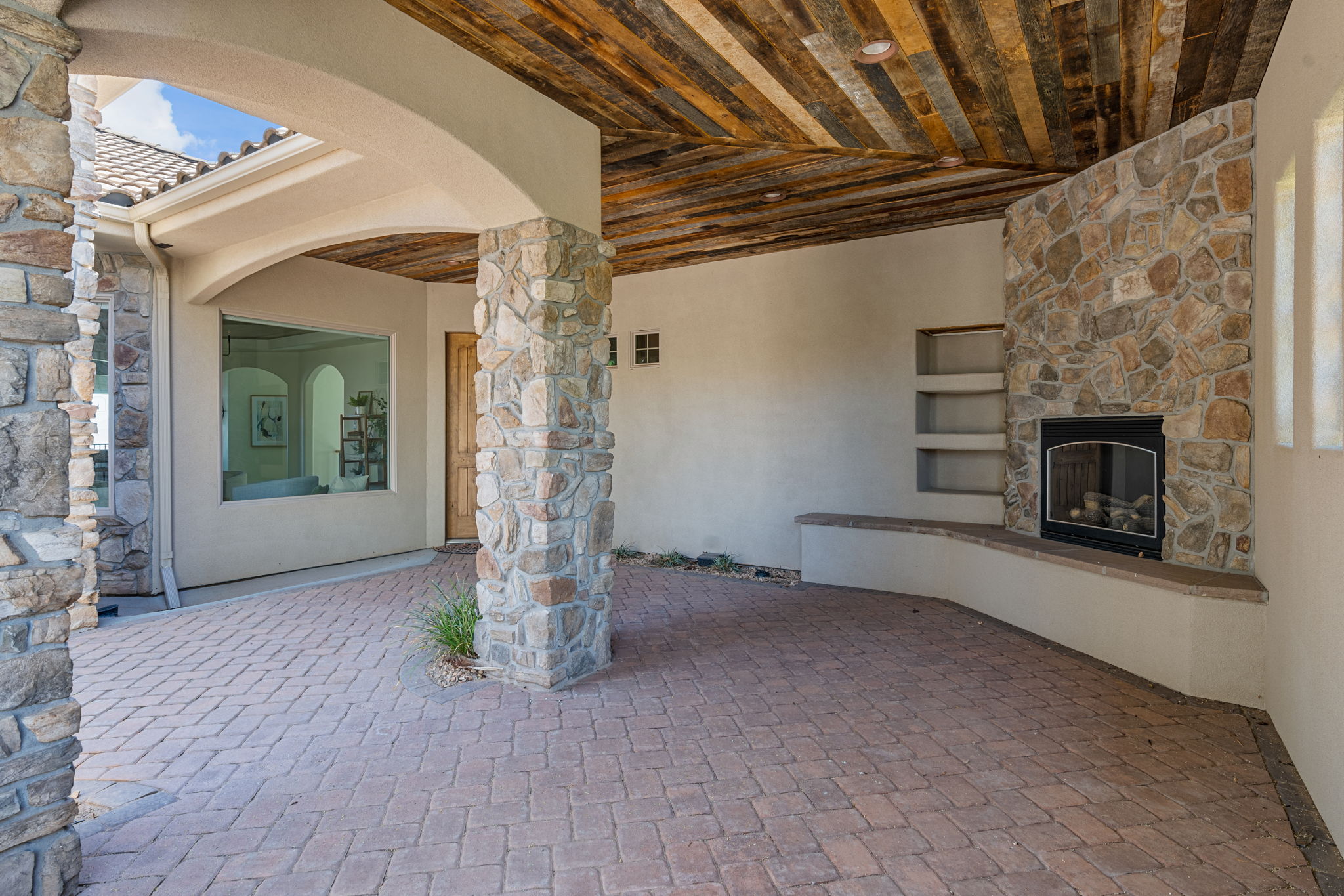 Covered patio featuring a stone fireplace, built-in shelving, and a wood-paneled ceiling