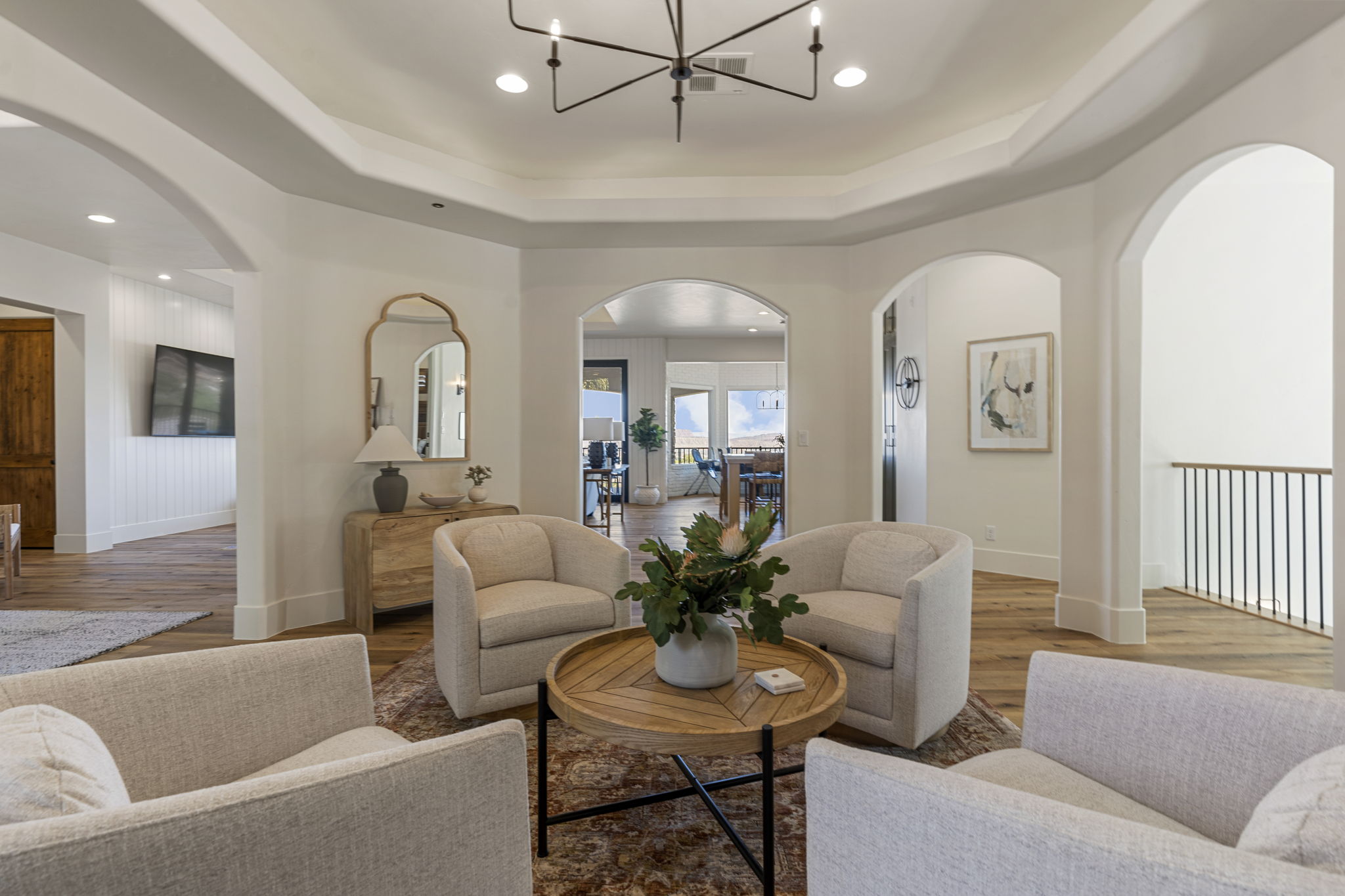 Open living area featuring wood-finish flooring, a tray ceiling with a contemporary chandelier, and multiple arched doorways