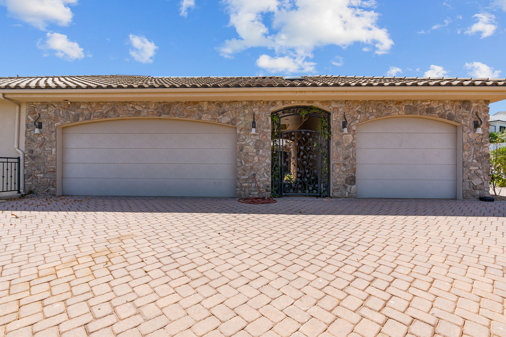 Paved driveway leading to a stone facade garage with two garage doors and a decorative wrought iron gate